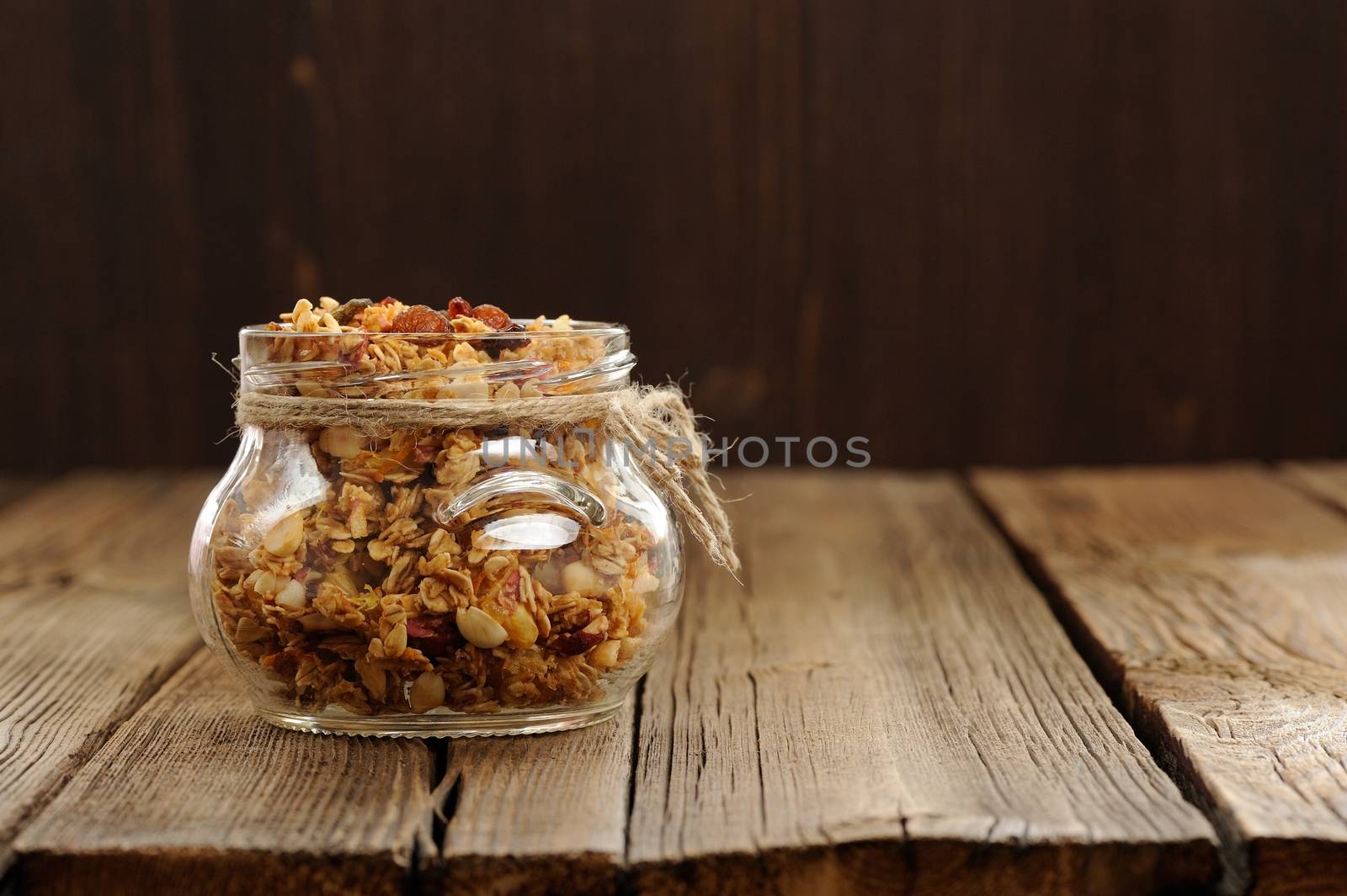Granola in jar with packing-twine on wooden background with space horizontal