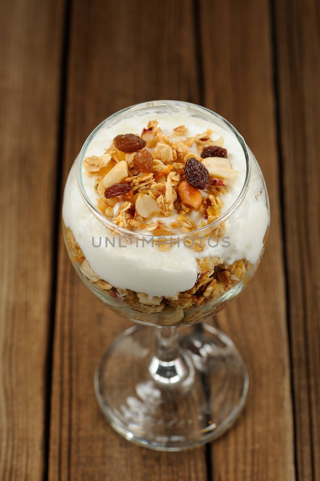 Granola in glass with yogurt on wooden background vertical