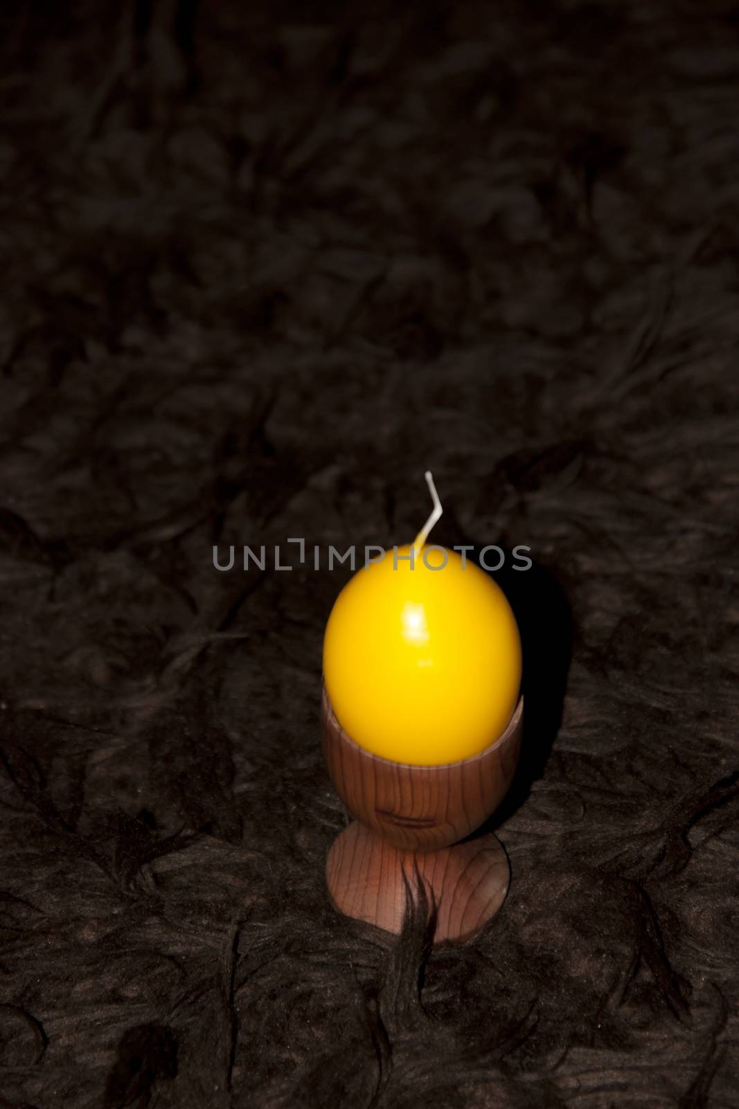 unlit yellow egg shaped candle in an egg cup on a brown carpet