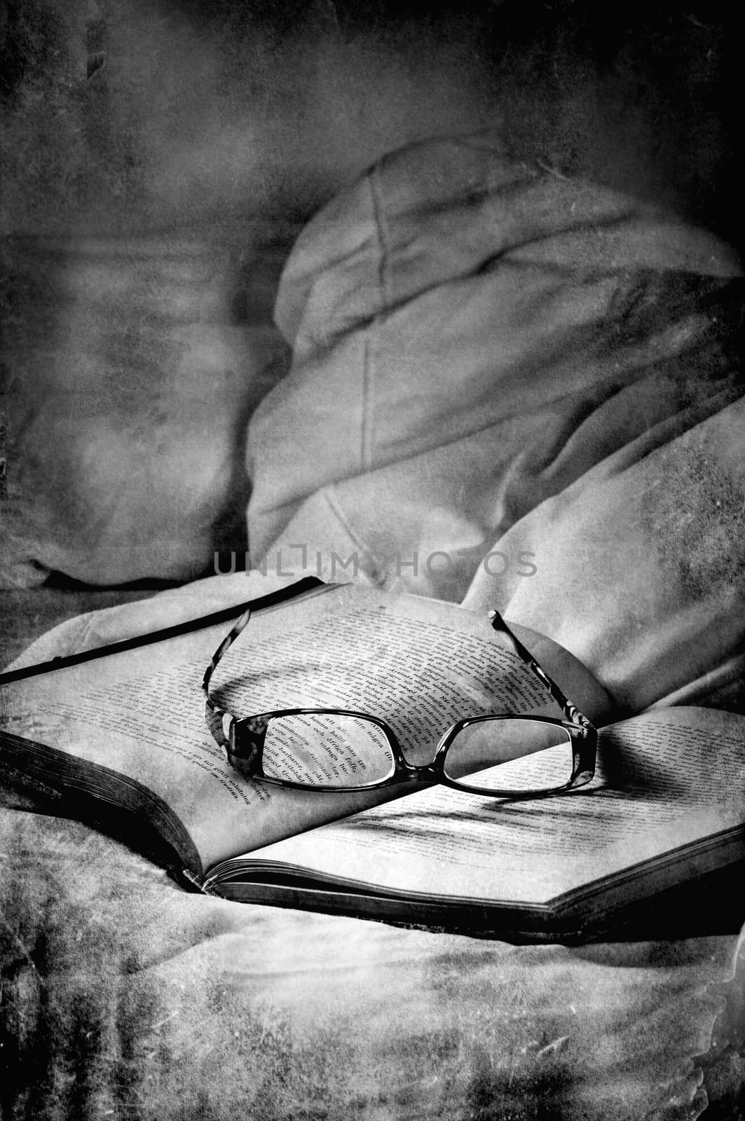 Dark textured image of book with glasses on a bed, scary feeling.