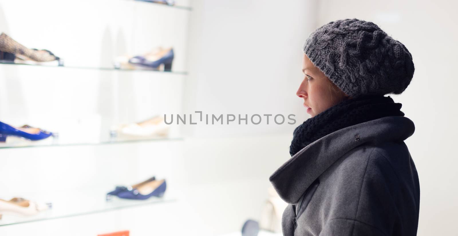 Casualy winter dressed lady window shopping in front of sinfully expensive boutique store dispaly window. Customer woman in shopping street, looking at window, outdoor.