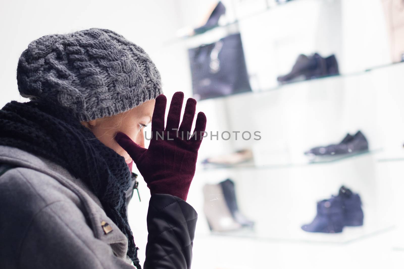 Casualy winter dressed lady window shopping in front of sinfully expensive boutique store dispaly window. Customer woman in shopping street, looking at window, outdoor.