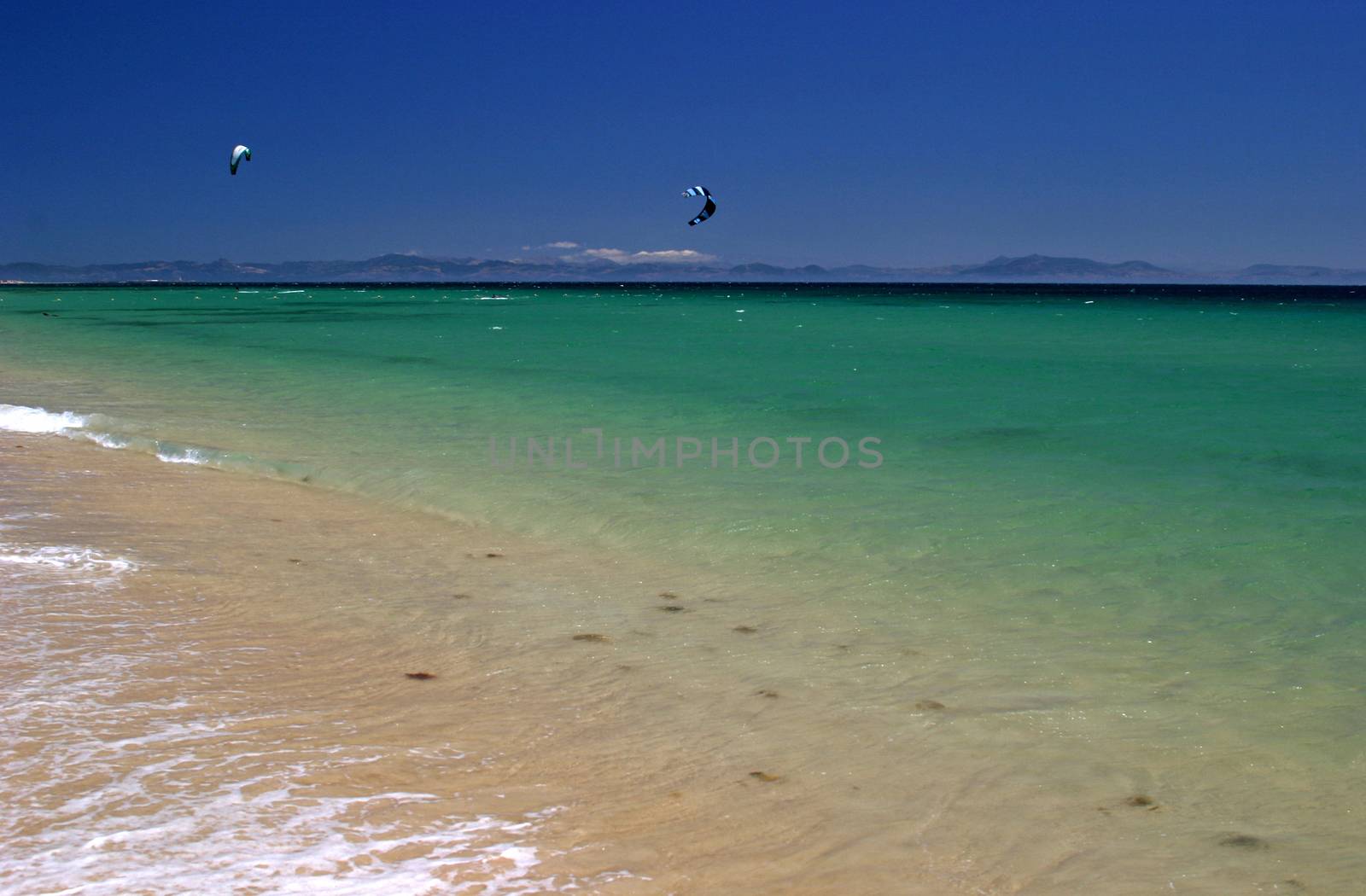 View Of Kite Surfers From A White Sandy Beach In Spain, Europe, On A Hot Sunny Day On Vacation.