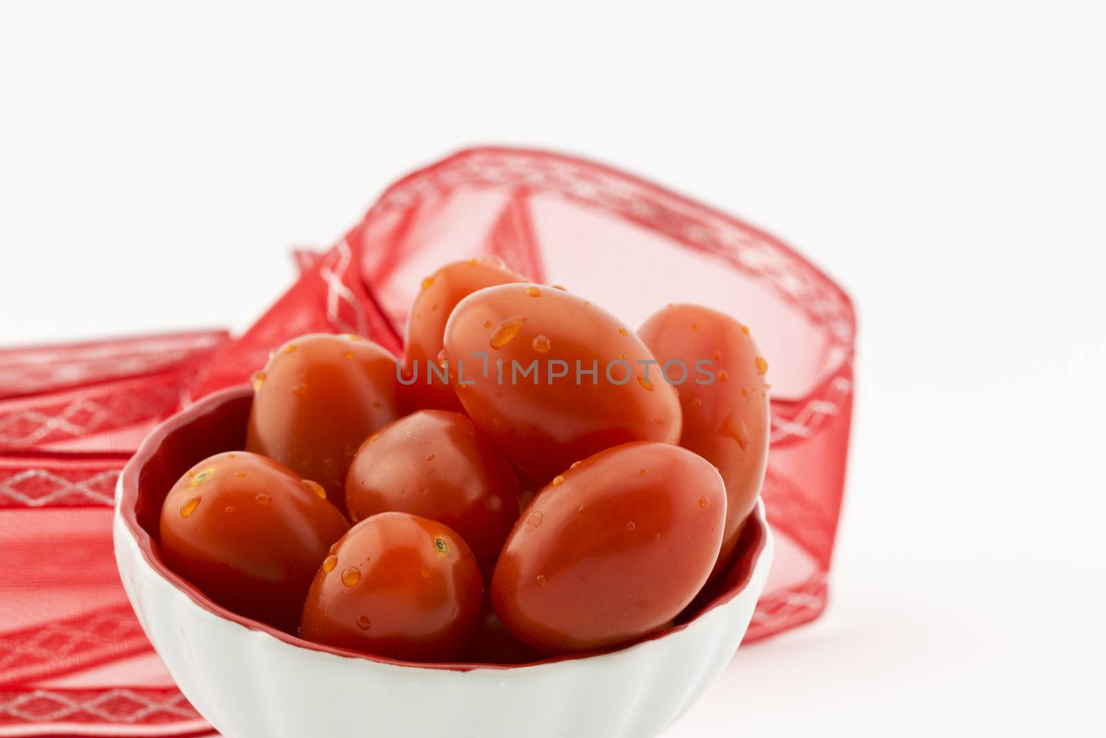 Fresh cherry tomatoes with water drops placed in white bowl with red ribbon behind