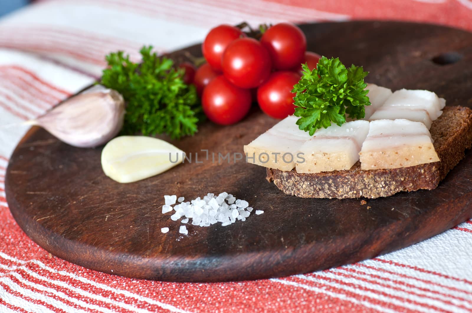 Sandwich made of salted lard on rye bread, served with garlic, cherry tomatoes and parsley
