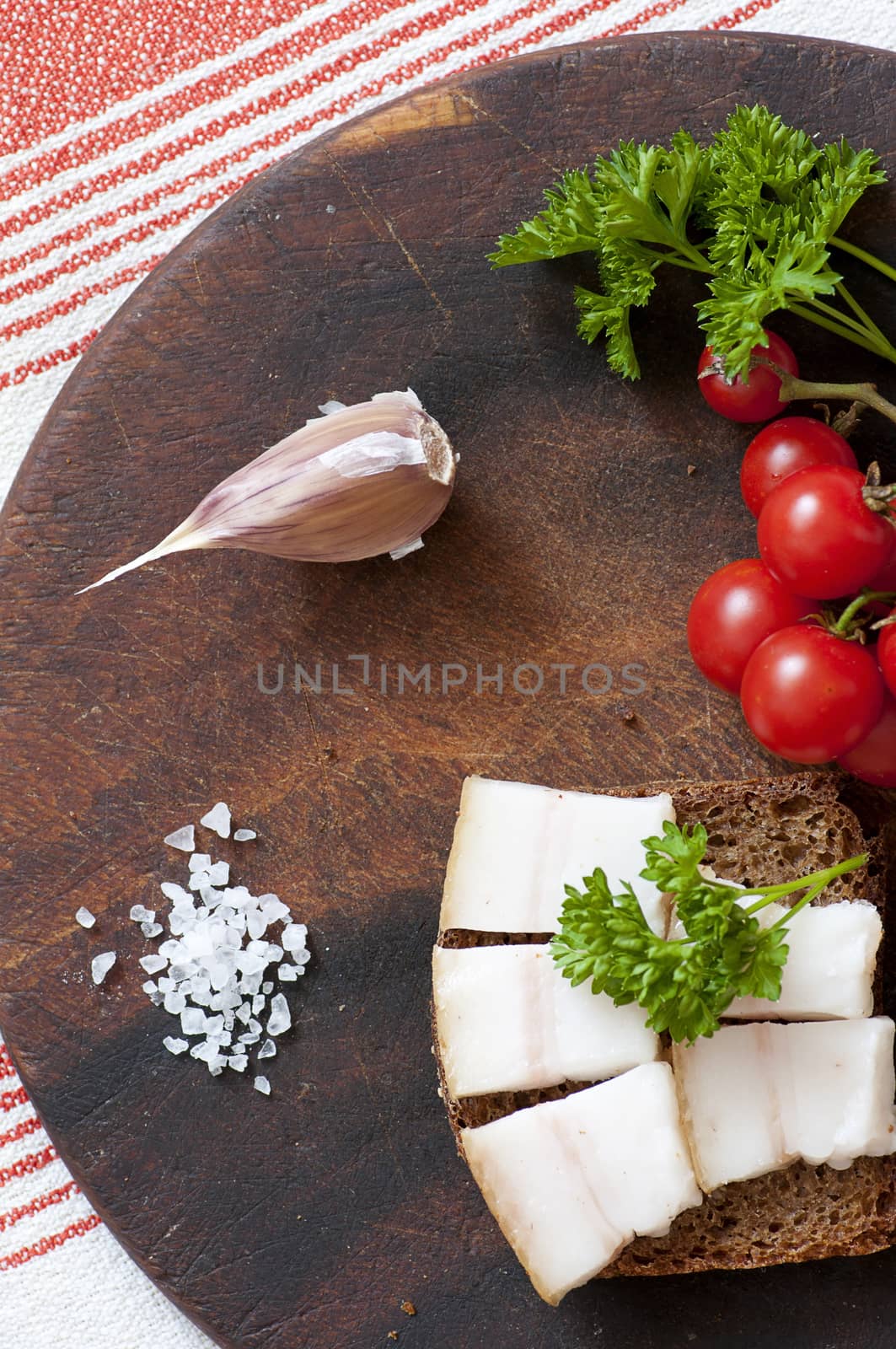 Sandwich made of salted lard on rye bread, served with garlic, cherry tomatoes and parsley