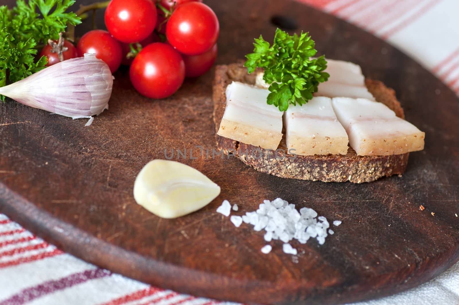 Sandwich made of salted lard on rye bread, served with garlic, cherry tomatoes and parsley