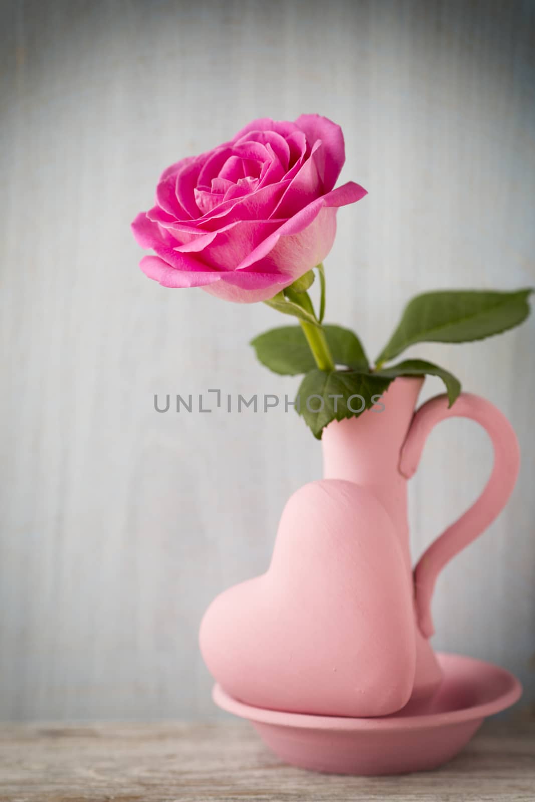 Pink roses in a vase with a Valentine's Day decoration on a wooden shelf.