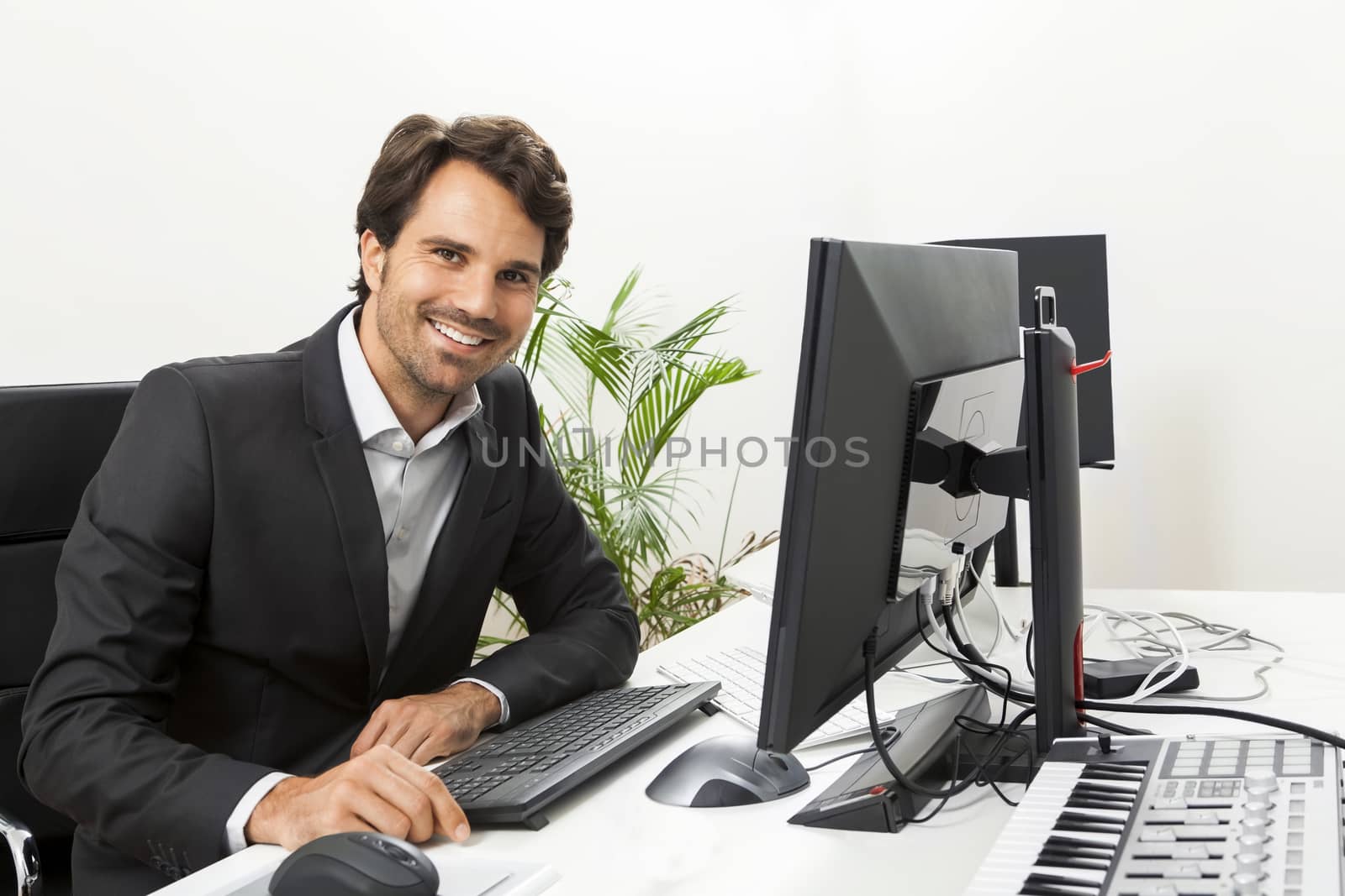 Stylish businessman in a suit sitting at his desk in the office chatting on the phone with a view of his blank computer monitor