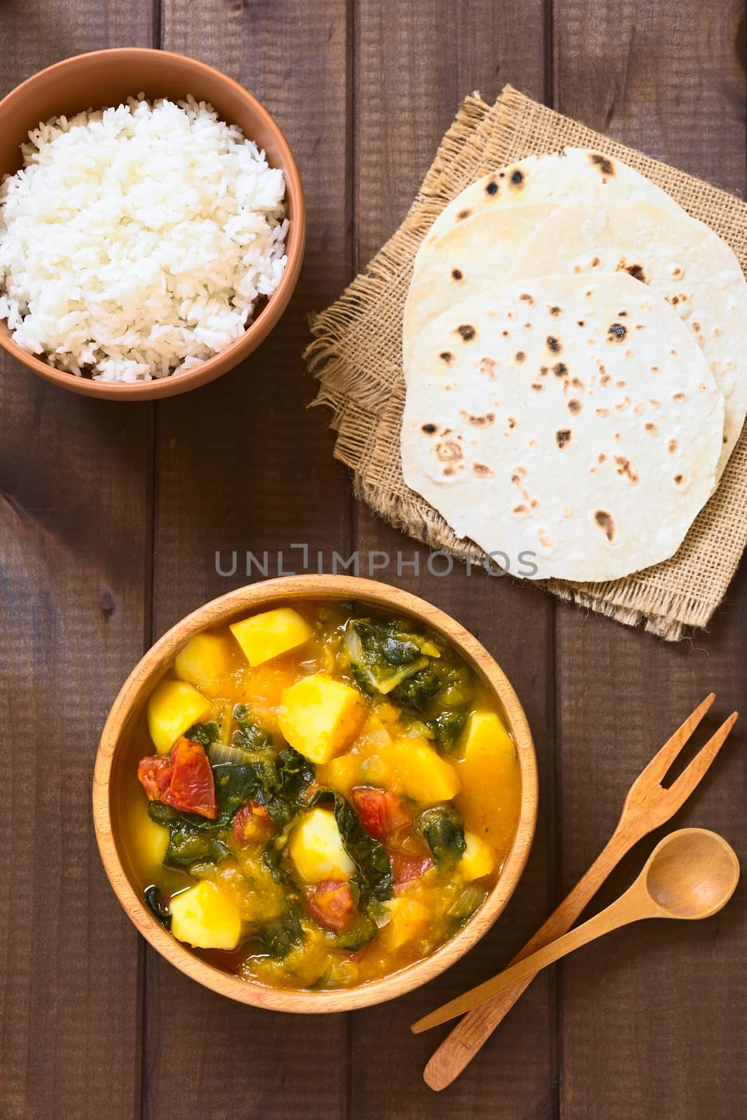 Overhead shot of pumpkin, mangold, potato and tomato curry dish in wooden bowl with homemade chapati flatbread and rice photographed with natural light