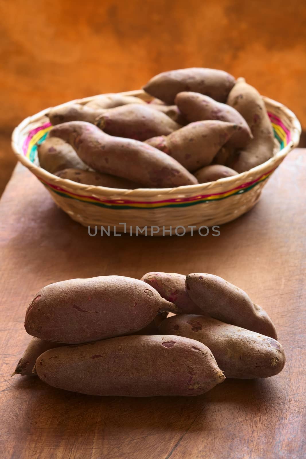 Pile of raw purple sweet potato (lat. Ipomoea batatas) on wooden board photographed with natural light (Selective Focus, Focus on the front of the sweet potato)