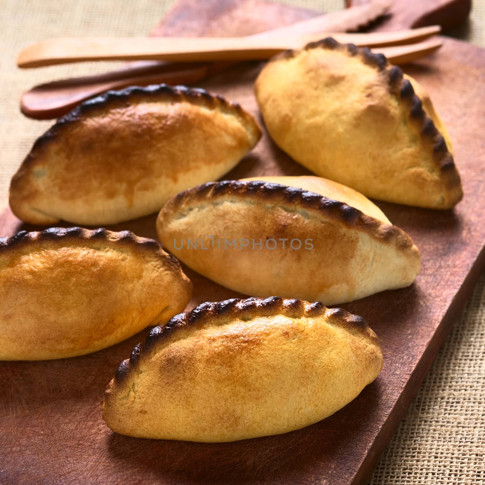 Traditional Bolivian savory pastries called Saltena filled with thick meat stew, which is a very popular street snack in Bolivia photographed on wood with natural light (Selective Focus, Focus on the first saltena)