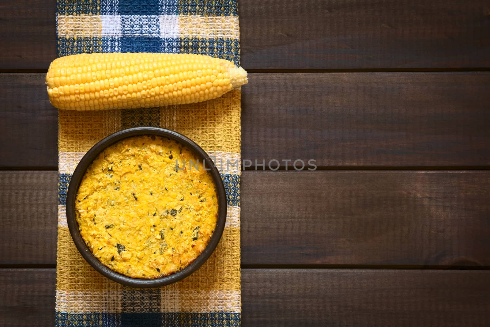 Overhead shot of traditional Chilean corn pie called Pastel de Choclo served in bowl, photographed on dark wood  with natural light. Below the corn-basil mix is ground meat, olive, boiled egg, raisins and pieces of chicken.   