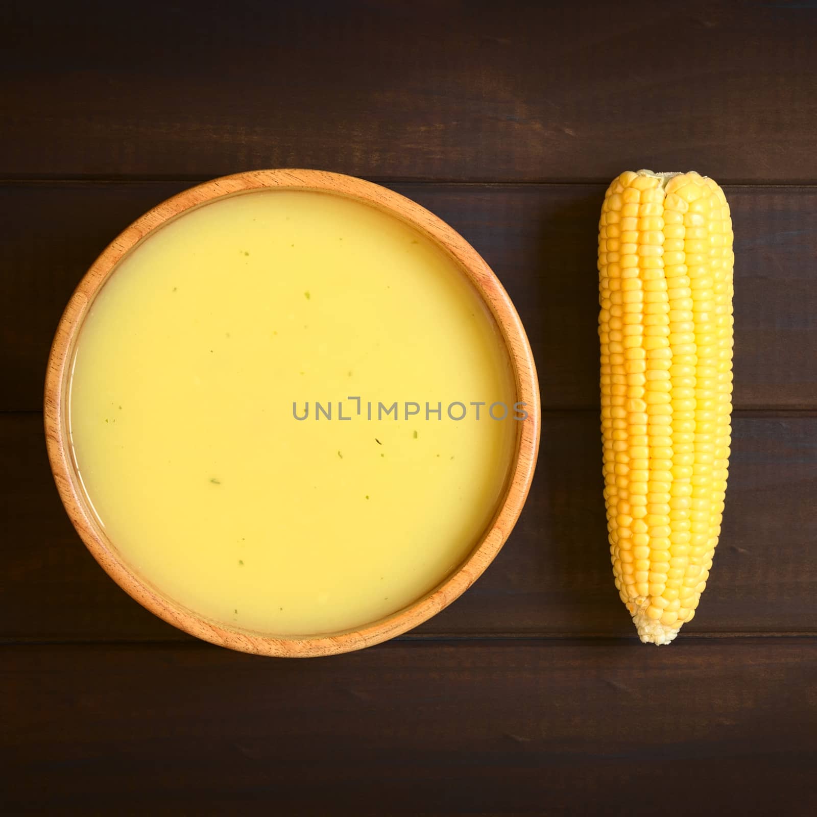 Overhead shot of cream of corn soup in wooden bowl with corn cob, photographed on dark wood with natural light