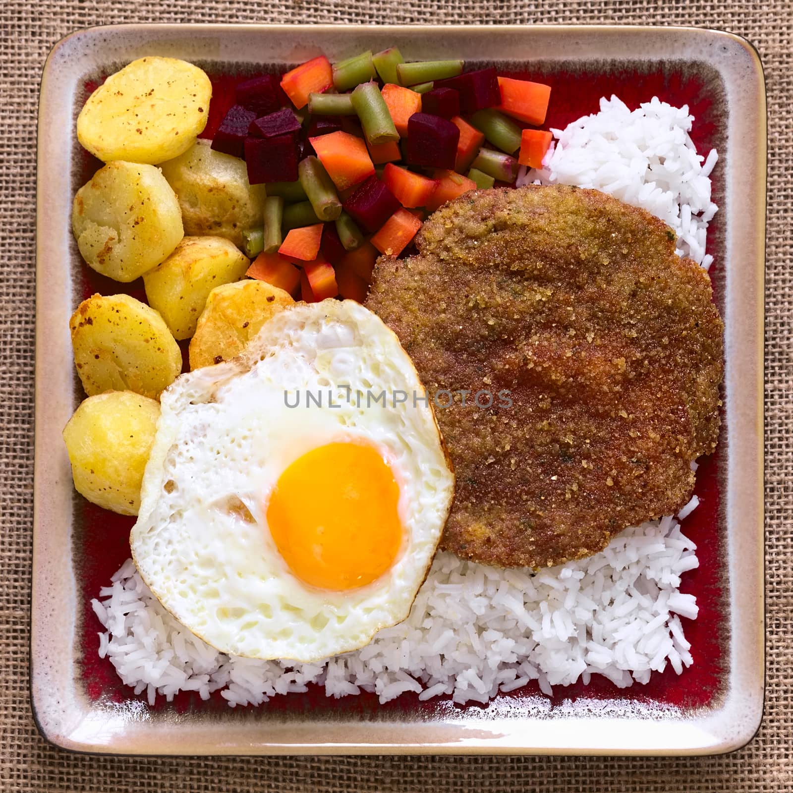 Overhead shot of traditional Bolivian dish called Silpancho, which is the name of the breaded flat, round piece of beef meat, served with fried egg, rice, fried potatoes and vegetables (carrot, bean, beetroot), photographed with natural light