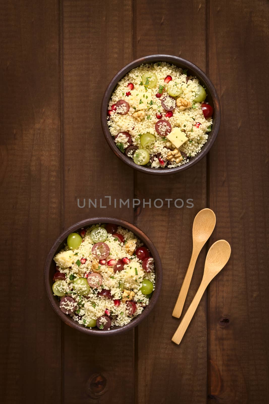 Overhead shot of two bowls of vegetarian couscous salad with grapes, pomegranate, walnuts, cheese, lime and mint, photographed with natural light