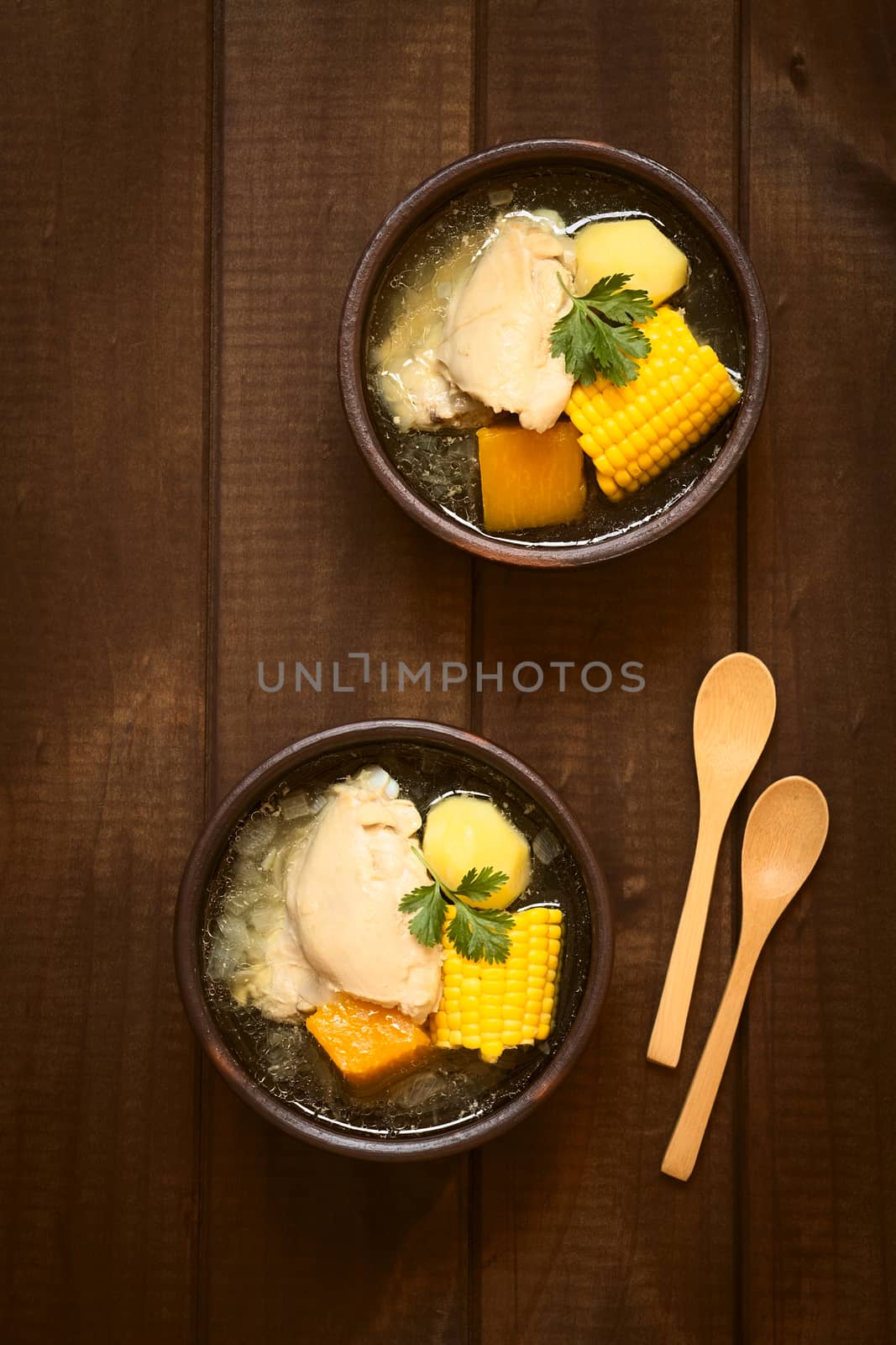 Overhead shot of two bowls of traditional Chilean Cazuela de Pollo (or Cazuela de Ave) soup made of chicken, sweetcorn, pumpkin and potato, garnished with fresh coriander, photographed on dark wood with natural light