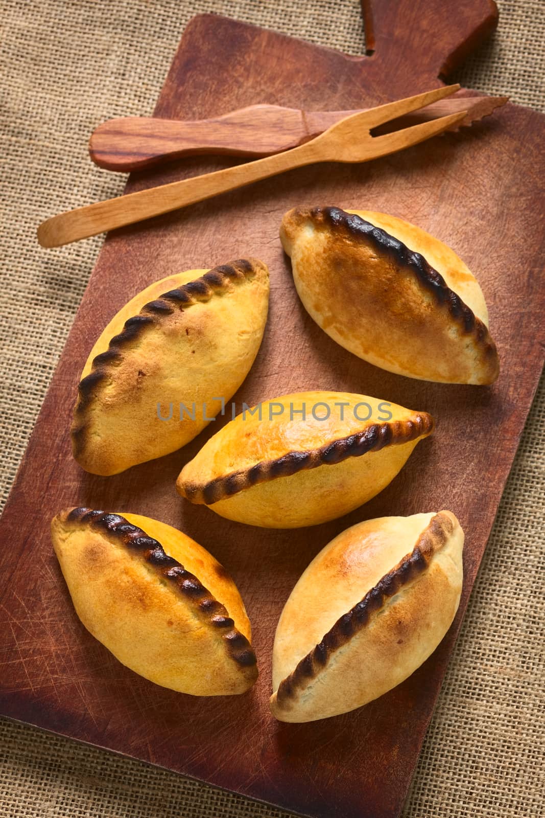 Traditional Bolivian savory pastries called Saltena filled with thick meat stew, which is a popular street snack in Bolivia, photographed on wood with natural light (Selective Focus, Focus on the top of the saltenas)