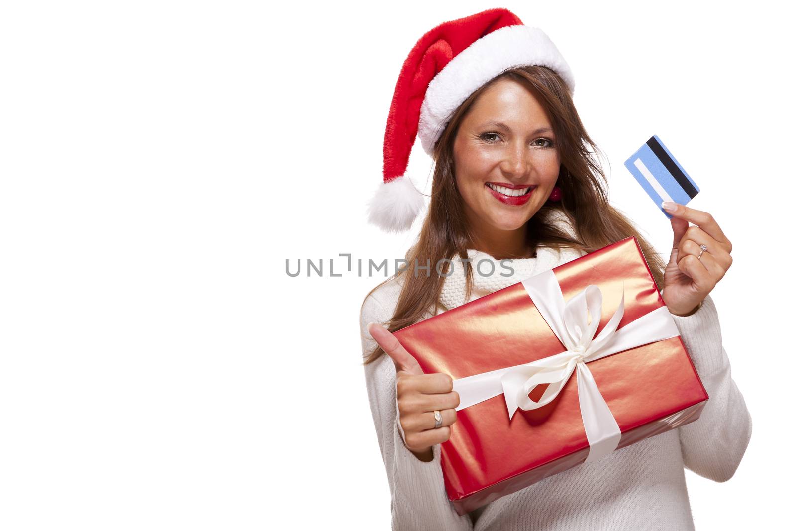 Smiling woman wearing a red Santa hat purchasing Christmas gifts on a bank card holding up a colorful red giftwrapped box with a happy smile and a thumbs up gesture of success, isolated on white