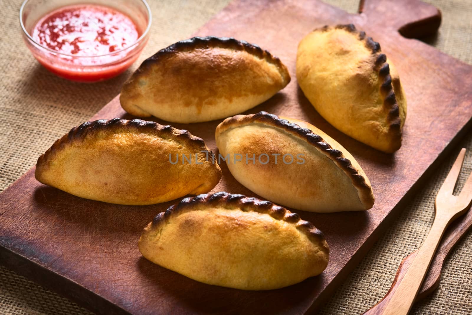 Traditional Bolivian savory pastries called Saltena filled with thick meat stew, which is a popular street snack in Bolivia, photographed on wood with natural light (Selective Focus, Focus on the saltenas in the middle)