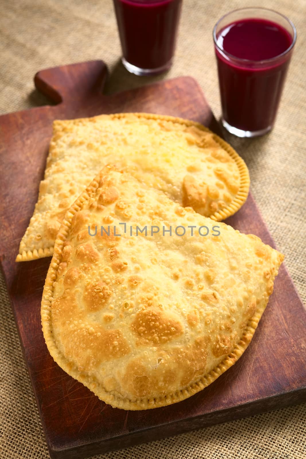 Traditional Bolivian Pastel, a deep-fried pastry filled with cheese, which is a popular street snack, served with api, a purple corn drink, photographed with natural light (Selective Focus, Focus on the lower half of the pastel)