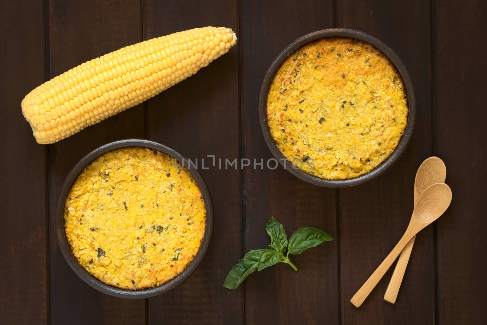 Overhead shot of traditional Chilean corn pie called Pastel de Choclo served in bowls, photographed on dark wood  with natural light. Below the corn-basil mix is ground meat, olive, boiled egg, raisins and pieces of chicken.   