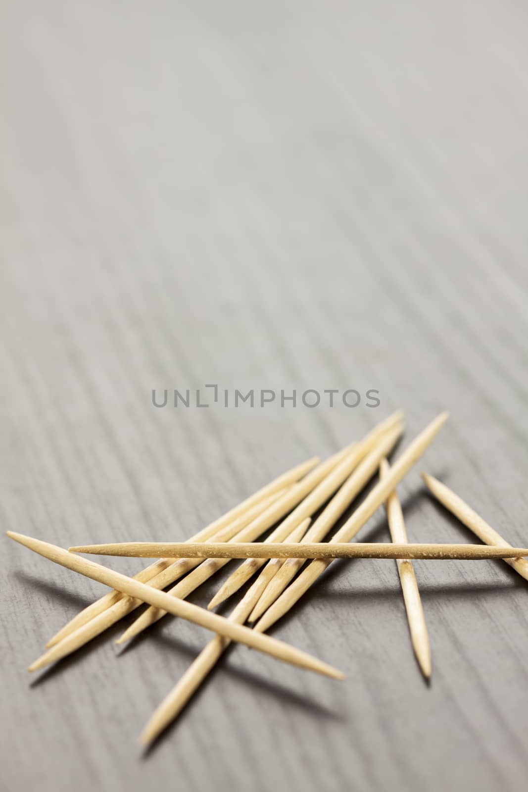 Pile of wooden toothpicks scattered randomly on a grey background for cleaning between the teeth after a meal in a personal hygiene concept