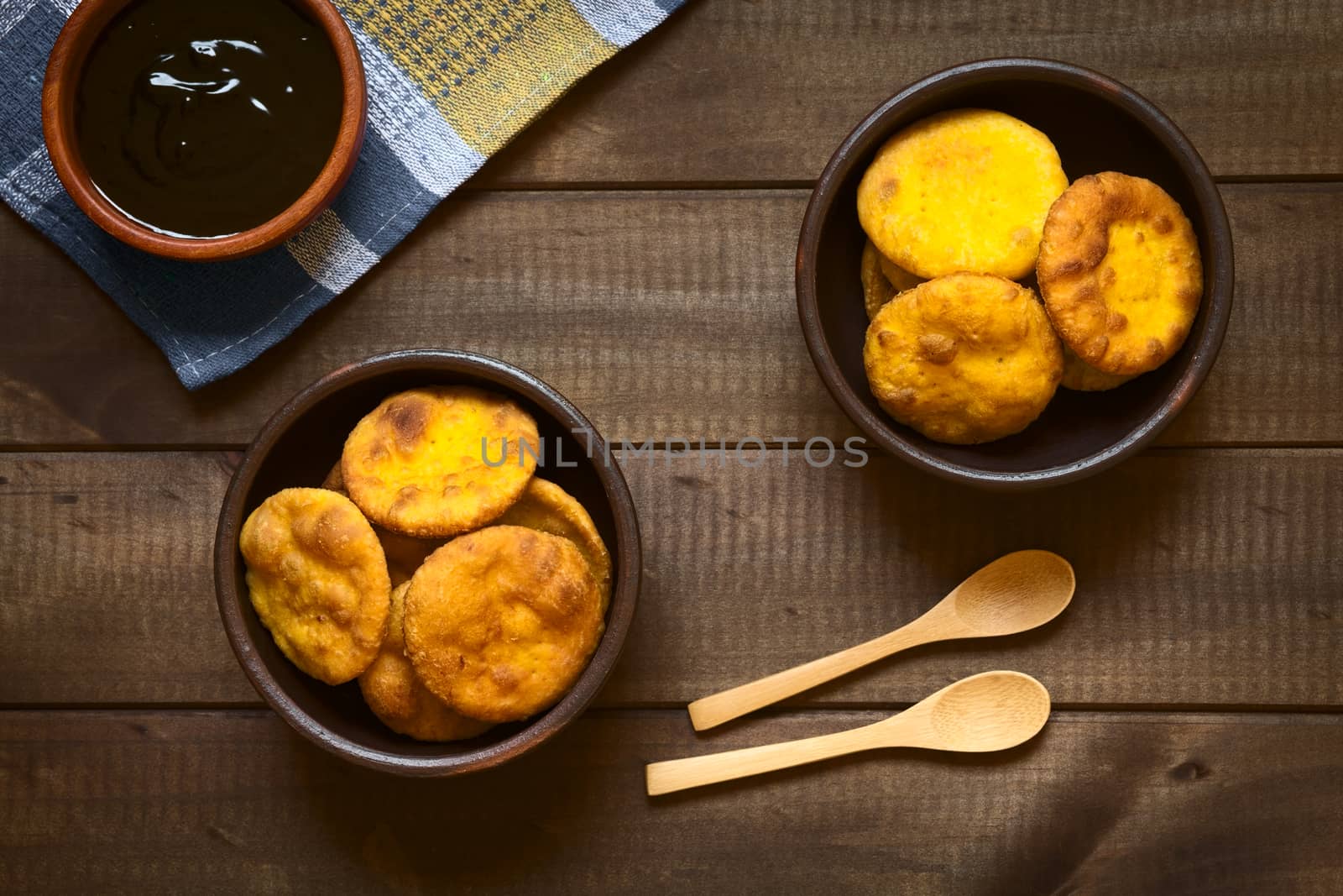 Overhead shot of traditional Chilean Sopaipilla fried pastry made with mashed pumpkin in the dough, served with Chancaca sweet sauce, photographed on dark wood with natural light