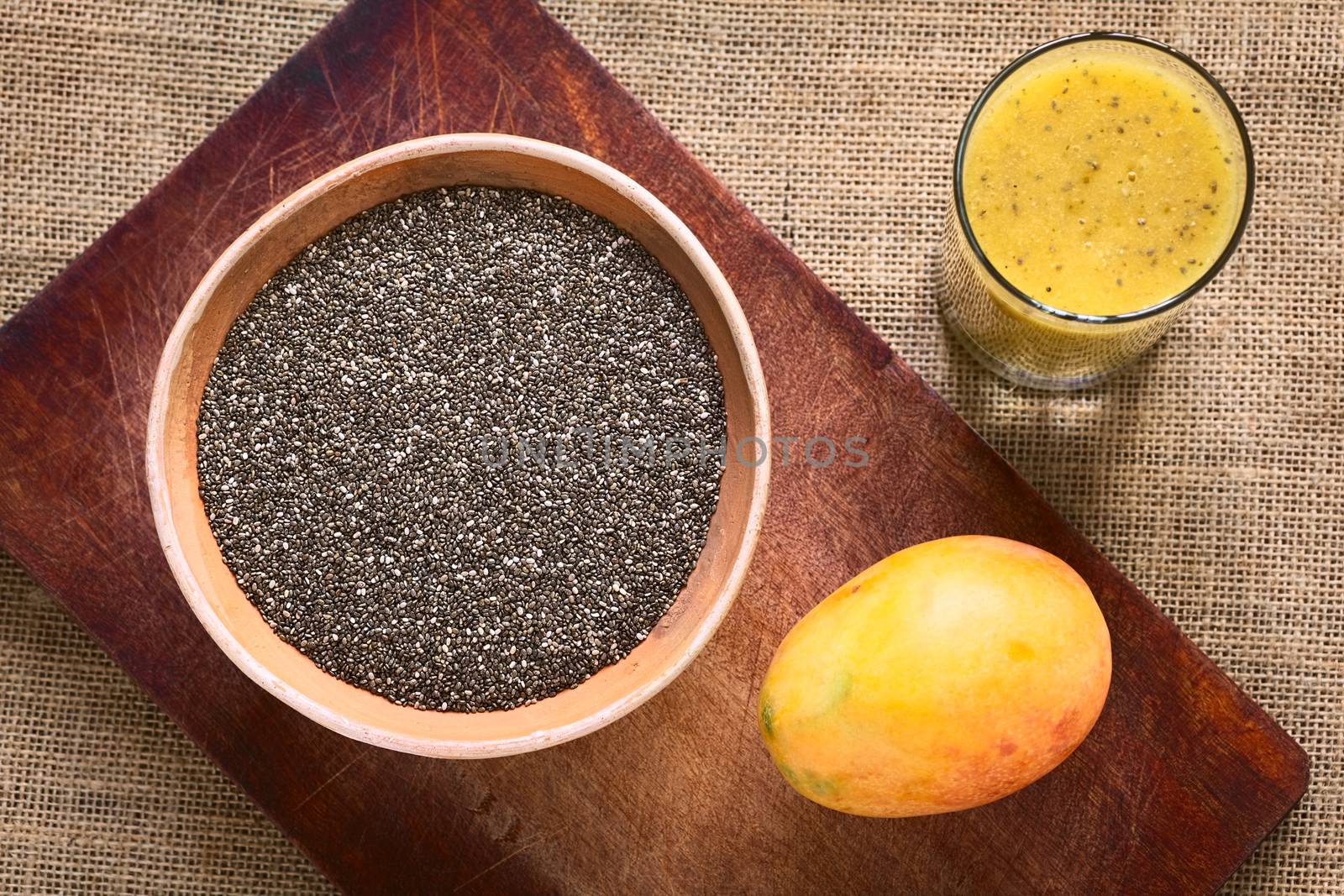 Overhead shot of chia seeds (lat. Salvia hispanica) in clay bowl with mango and mango-chia juice photographed with natural light. Chia seeds are considered a superfood containing proteins, omega fats, minerals and antioxidants