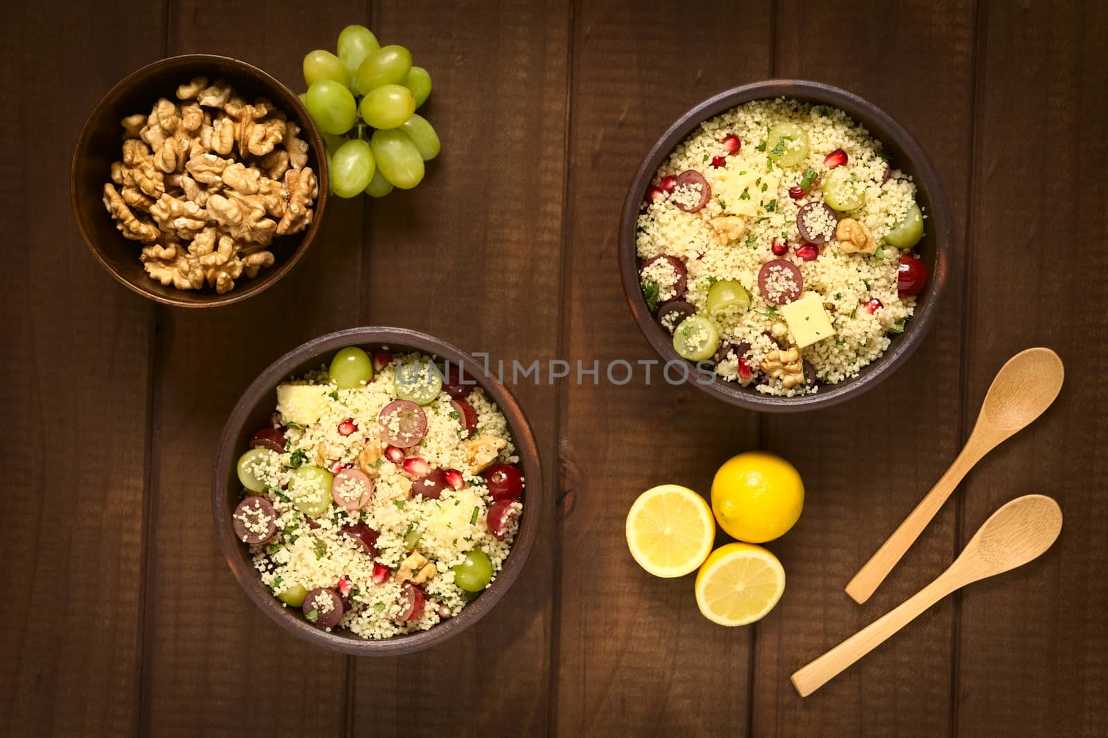 Overhead shot of two bowls of vegetarian couscous salad with grapes, pomegranate, walnuts, cheese, lime and mint, photographed with natural light
