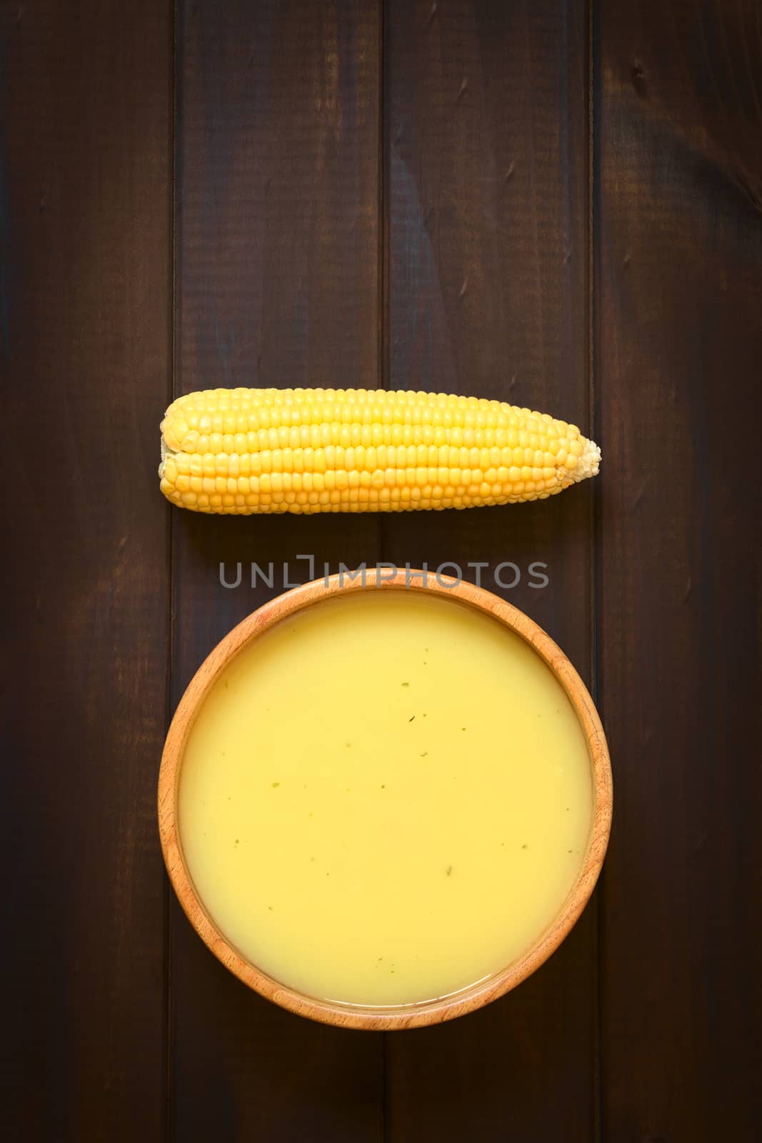 Overhead shot of cream of corn soup in wooden bowl with corn cob, photographed on dark wood with natural light