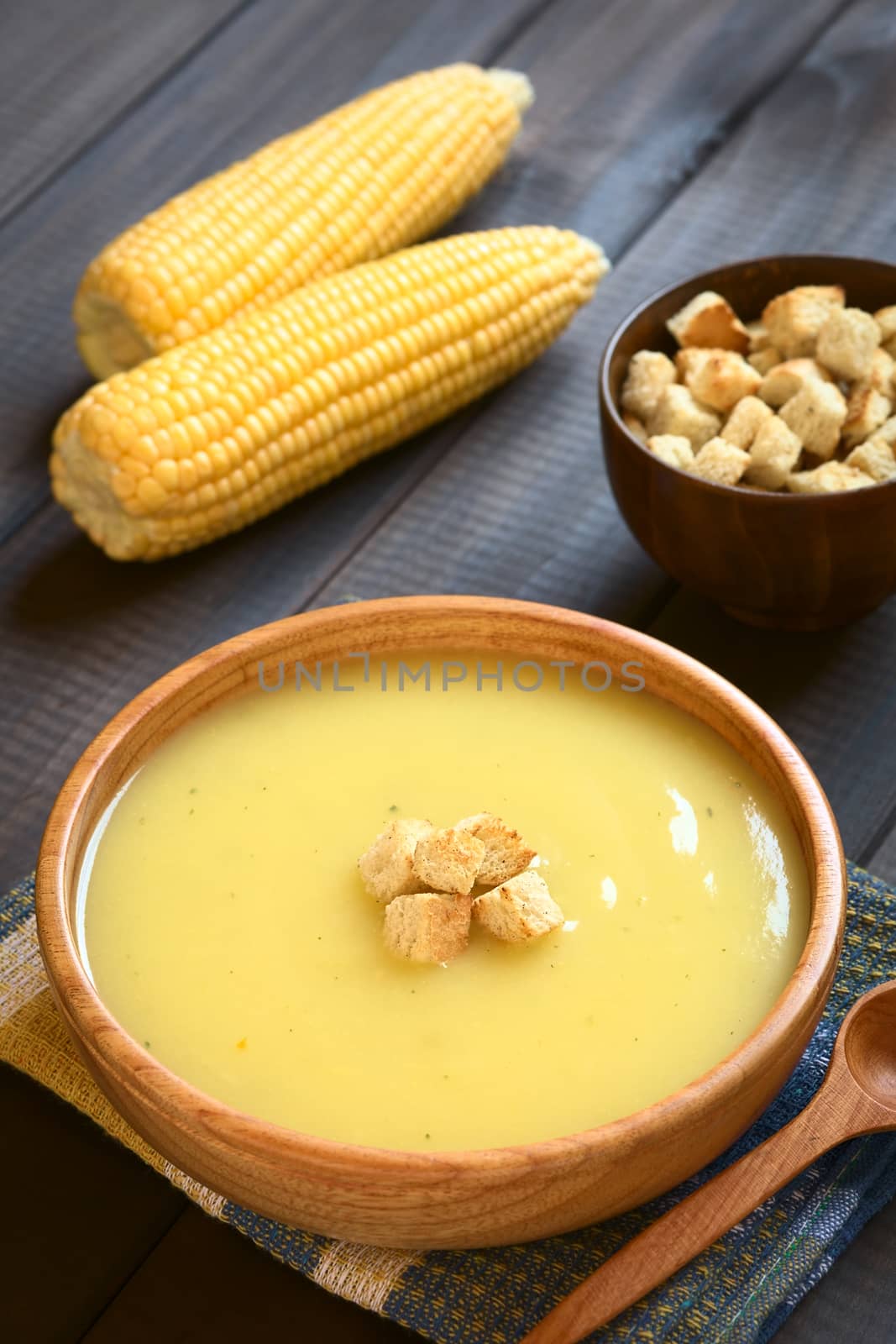 Cream of corn soup in wooden bowl with croutons on top, photographed on dark wood with natural light (Selective Focus, Focus on the front of the croutons on the soup)