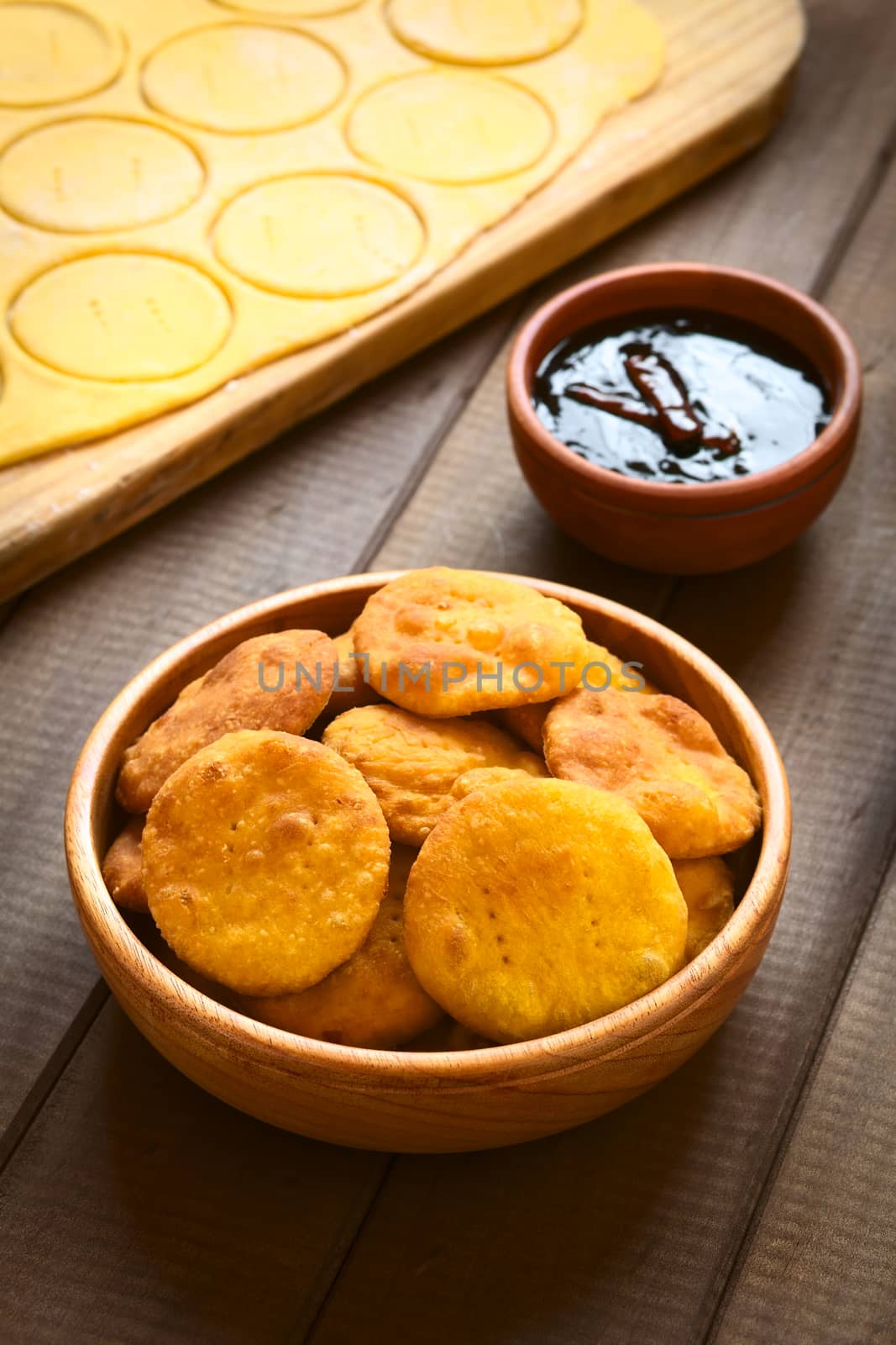 Traditional Chilean Sopaipilla fried pastry made with mashed pumpkin in the dough, served with Chancaca sweet sauce, photographed on wood with natural light (Selective Focus, Focus on the first two sopaipillas)