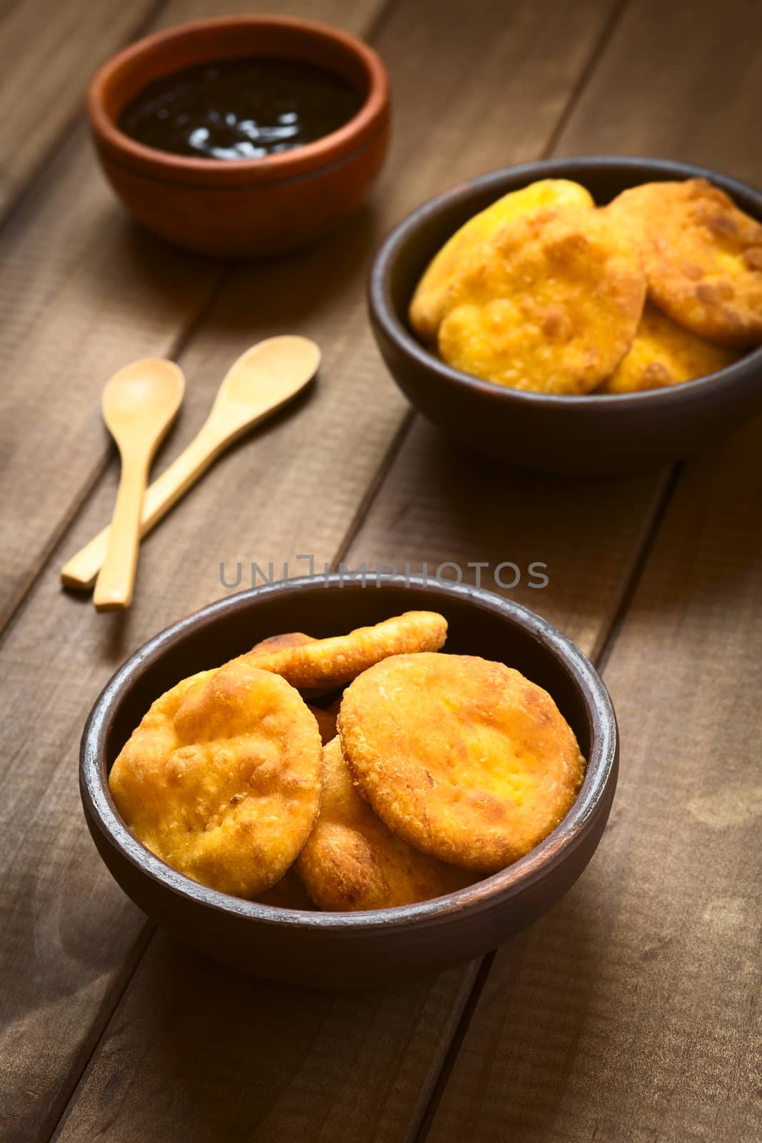 Traditional Chilean Sopaipilla fried pastry made with mashed pumpkin in the dough, served with Chancaca sweet sauce, photographed on dark wood with natural light (Selective Focus, Focus on the sopaipillas in the front)