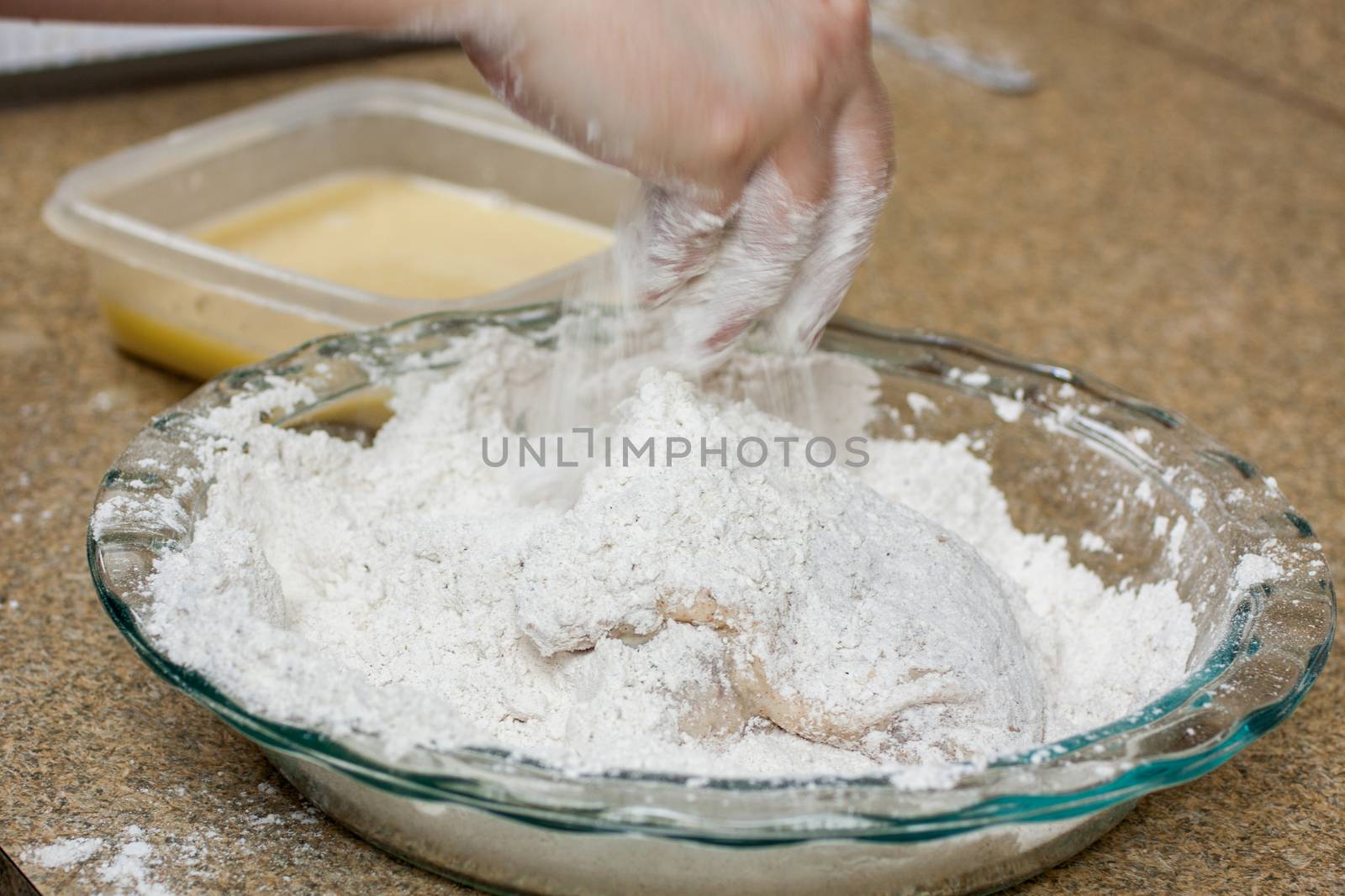 A woman coats fresh chicken in flour and egg wash in preperation for frying.