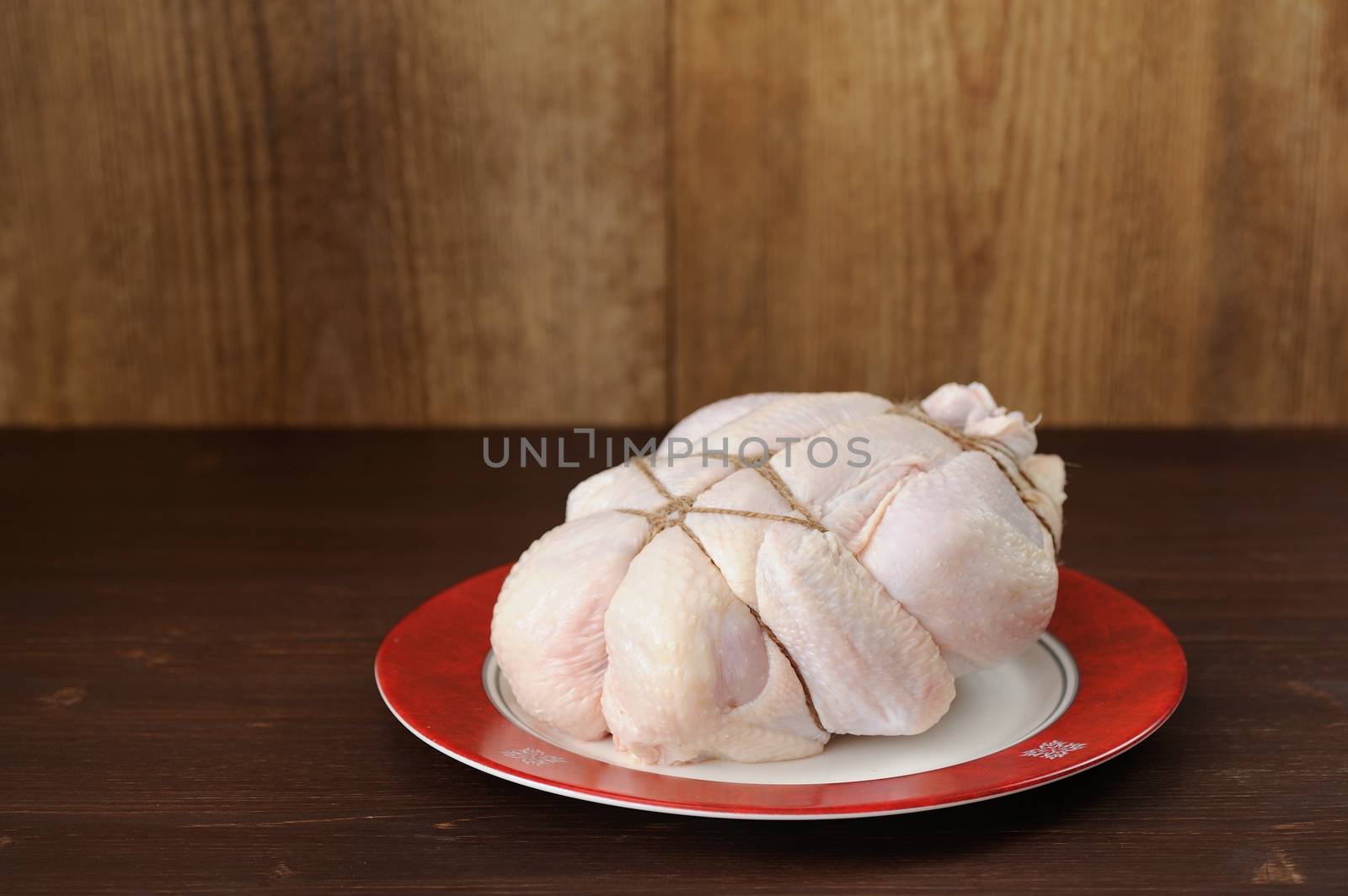 Bondage shibari raw chicken on red boarder plate on dark wood background with space horizontal