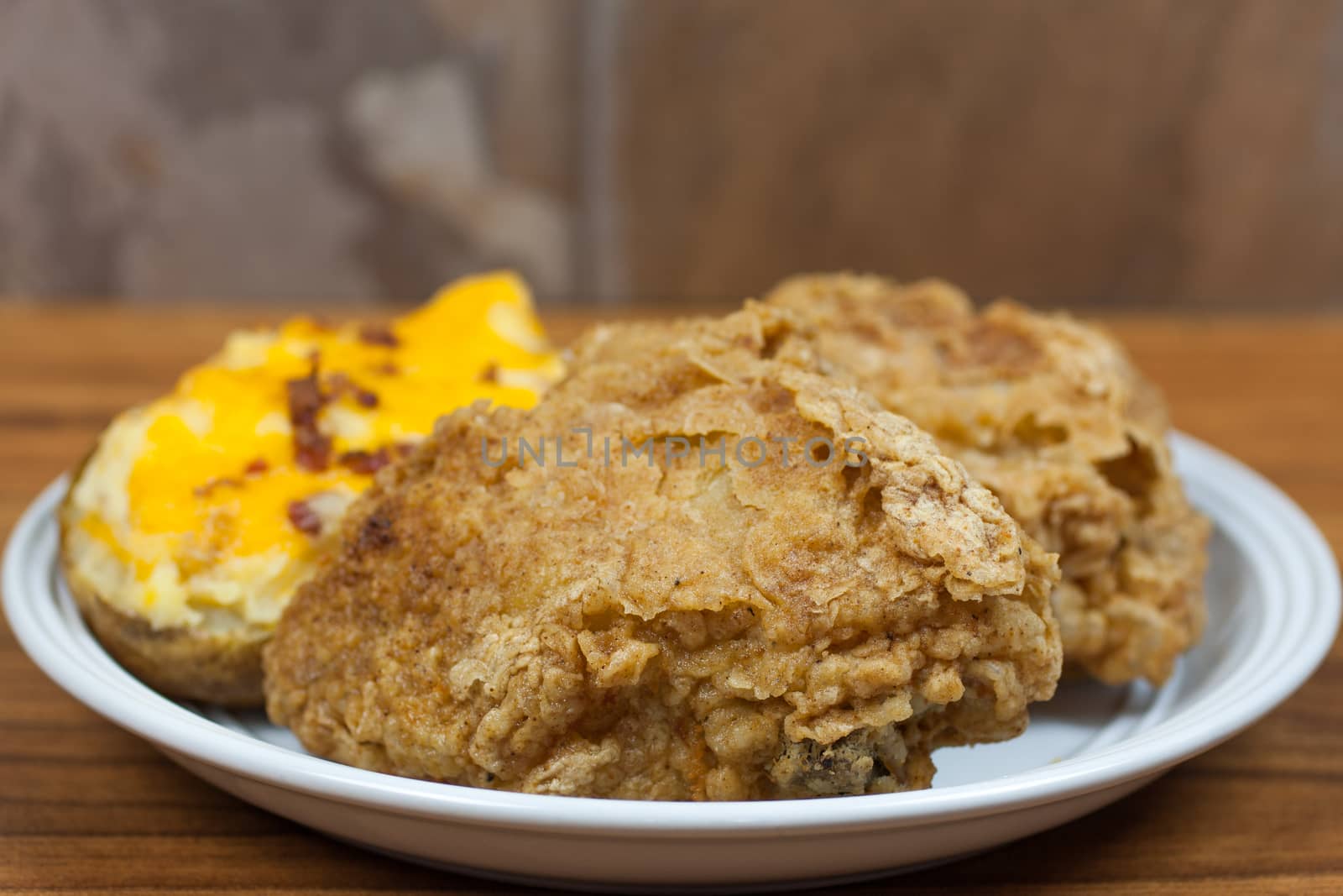 Crispy fried chicken on a plate with a twice baked potato with cheese and bacon.