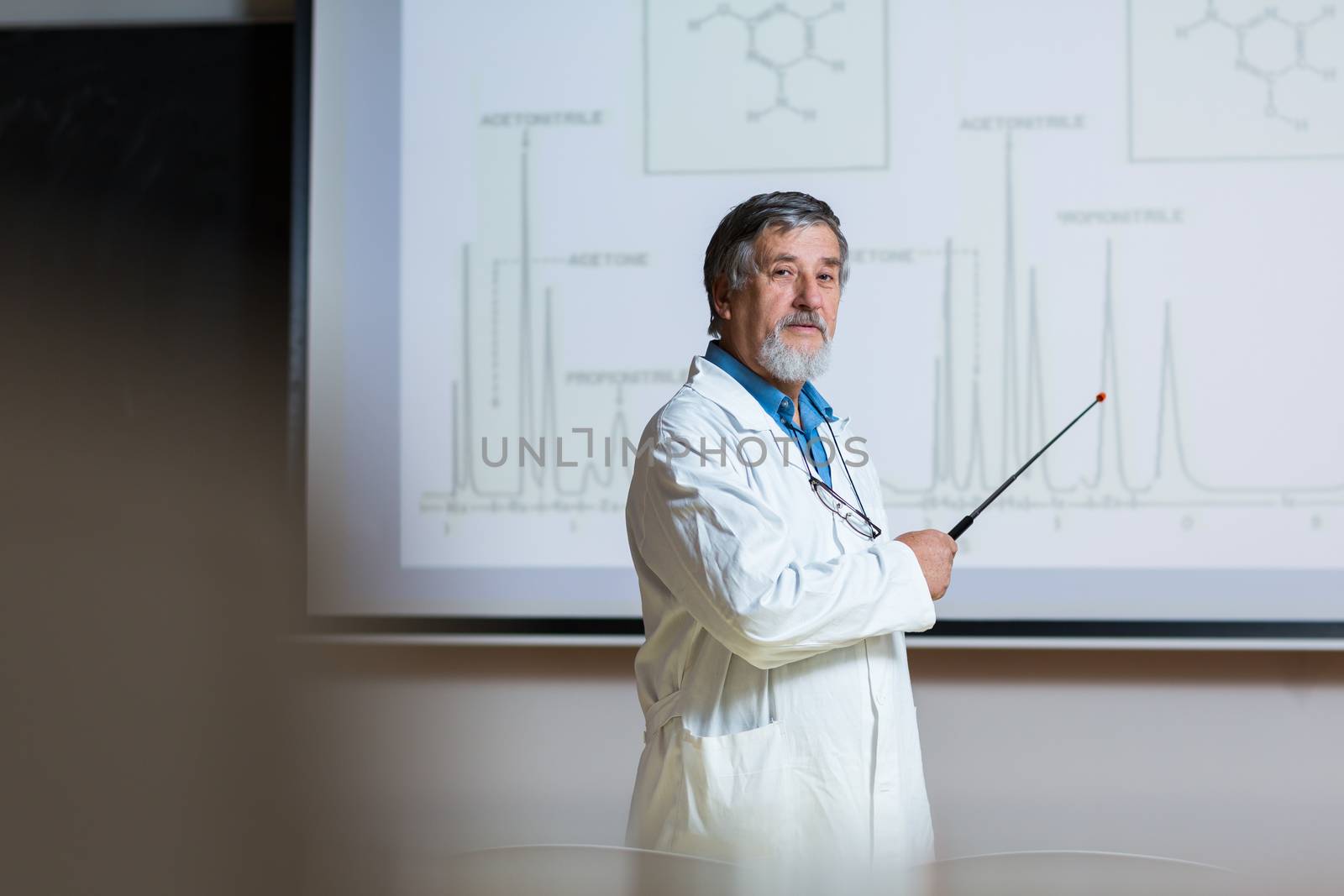 Senior chemistry professor giving a lecture in front of classroom full of students (shallow DOF; color toned image)