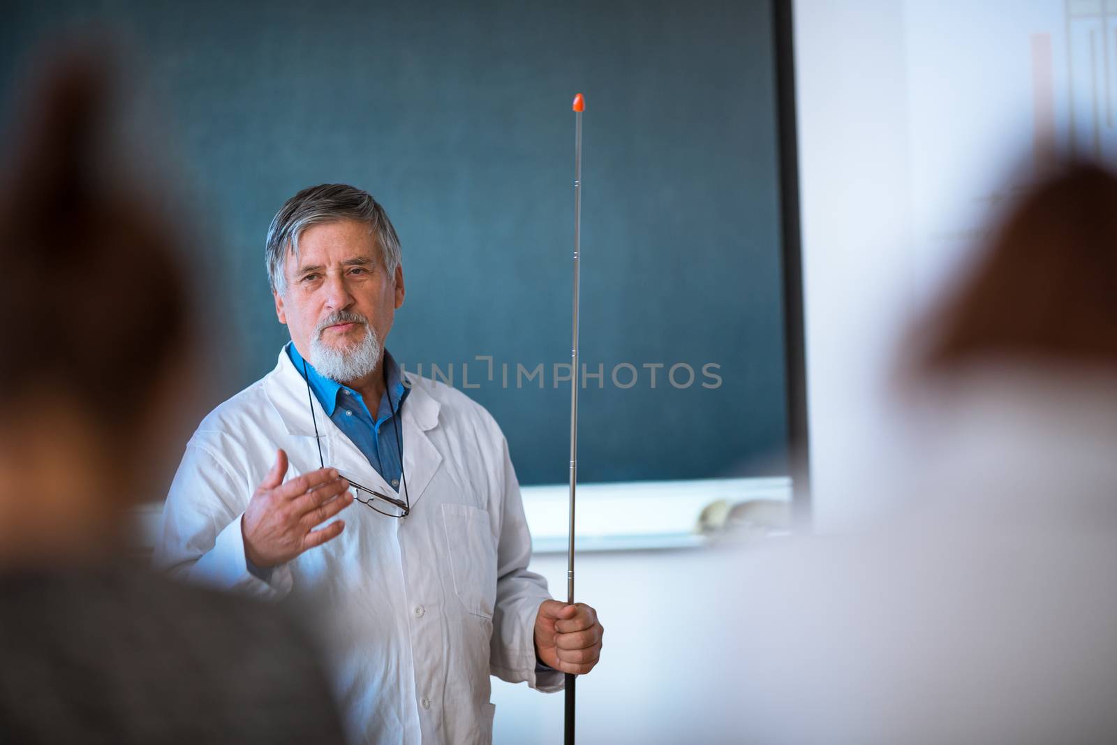 Senior chemistry professor giving a lecture in front of classroom full of students (shallow DOF; color toned image)