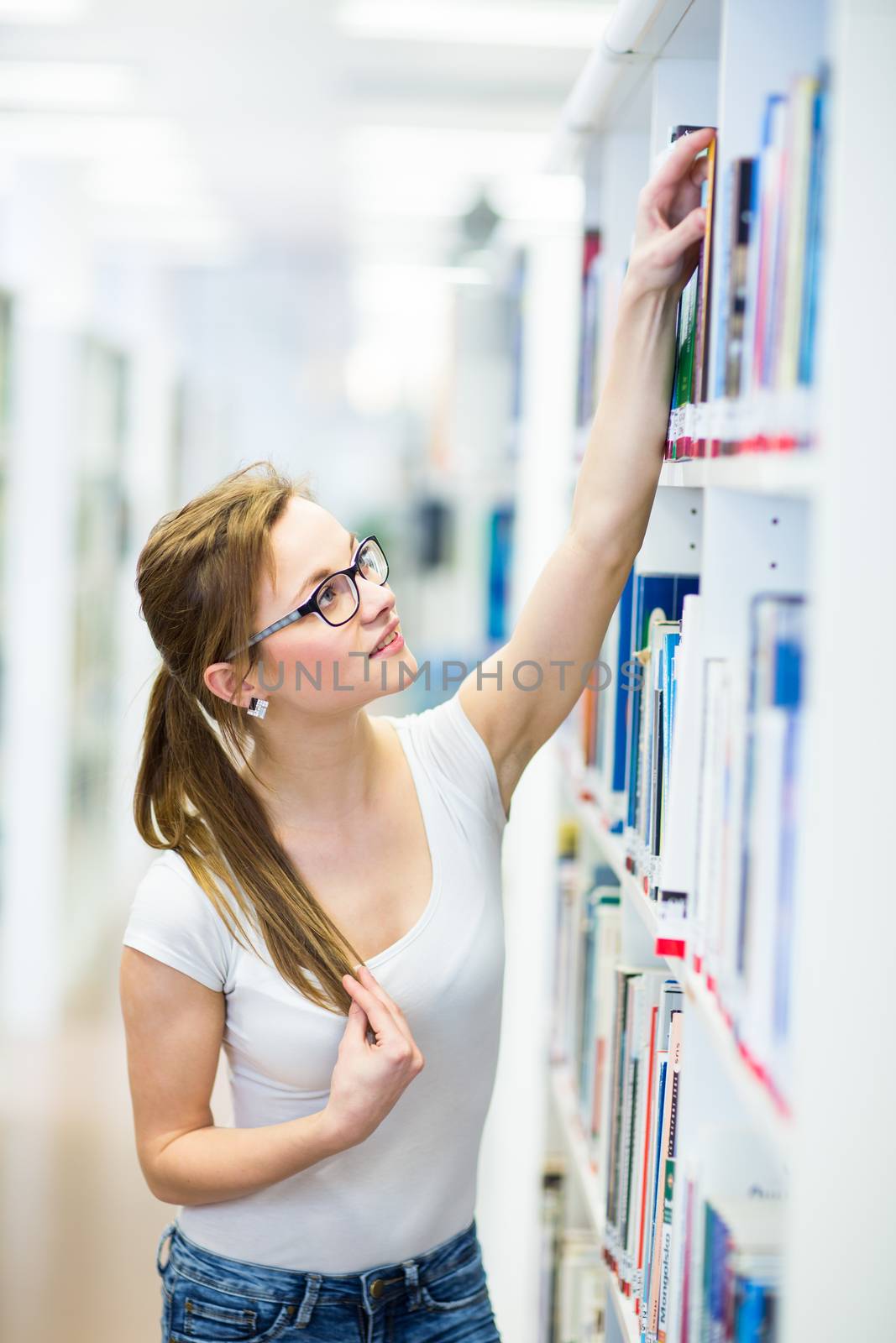 Pretty, female college student in a library, looking for a book  by viktor_cap