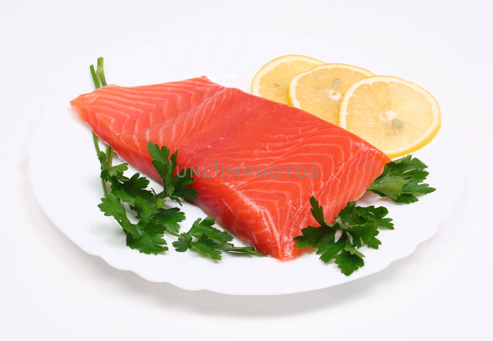 Salmon steak with lemon slices and parsley on white plate