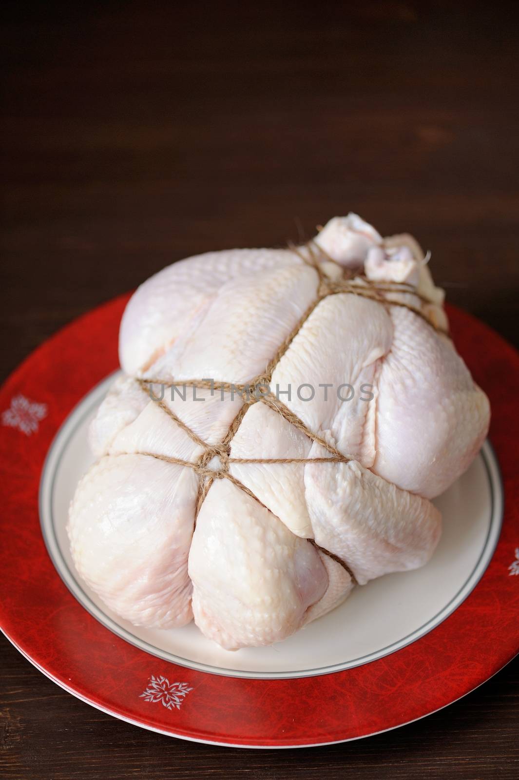 Bondage shibari raw chicken on red boarder plate on dark wood background vertical