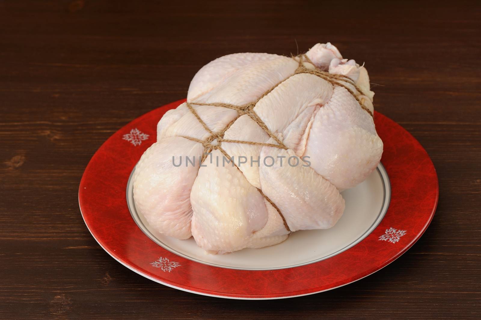 Bondage shibari raw chicken on red boarder plate on dark wood background horizontal
