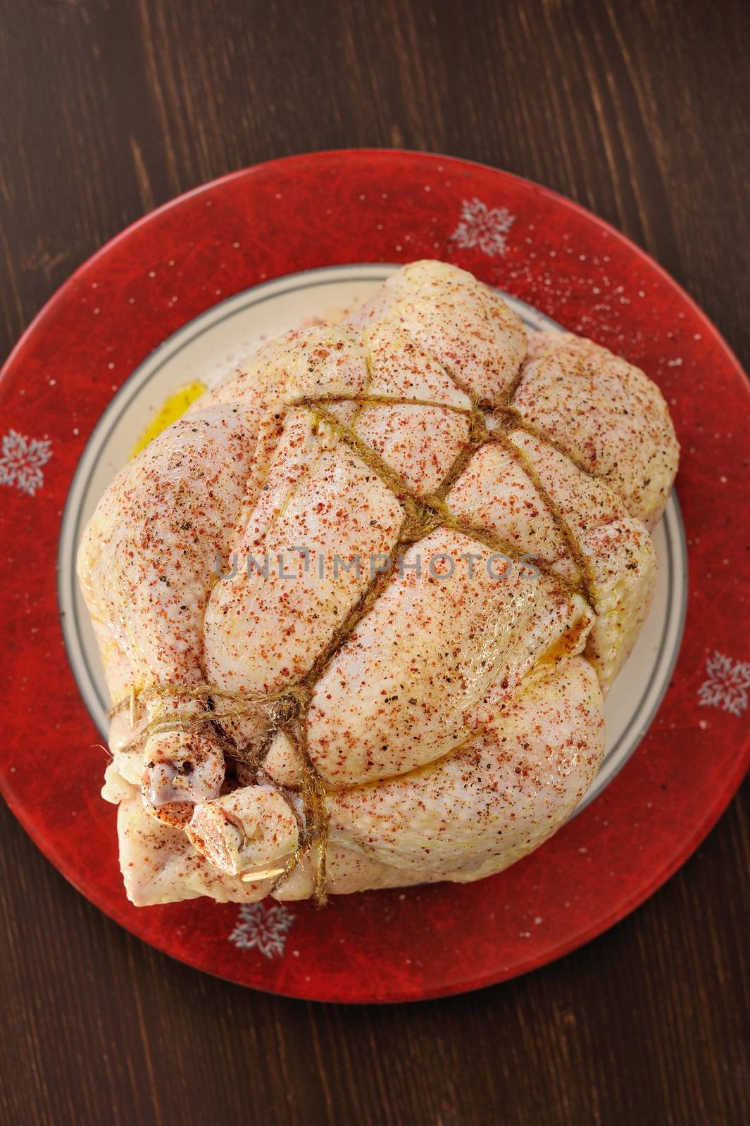 Bondage shibari oiled and spiced raw chicken on red boarder plate on dark wood background top view closup verticalselective focus