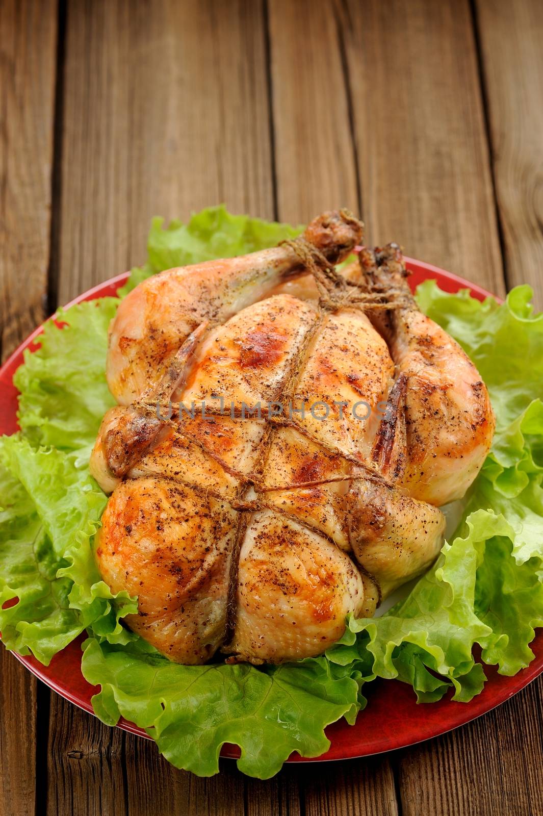 Bondage shibari roasted chicken with salad leaves on red plate on wooden background with space vertical