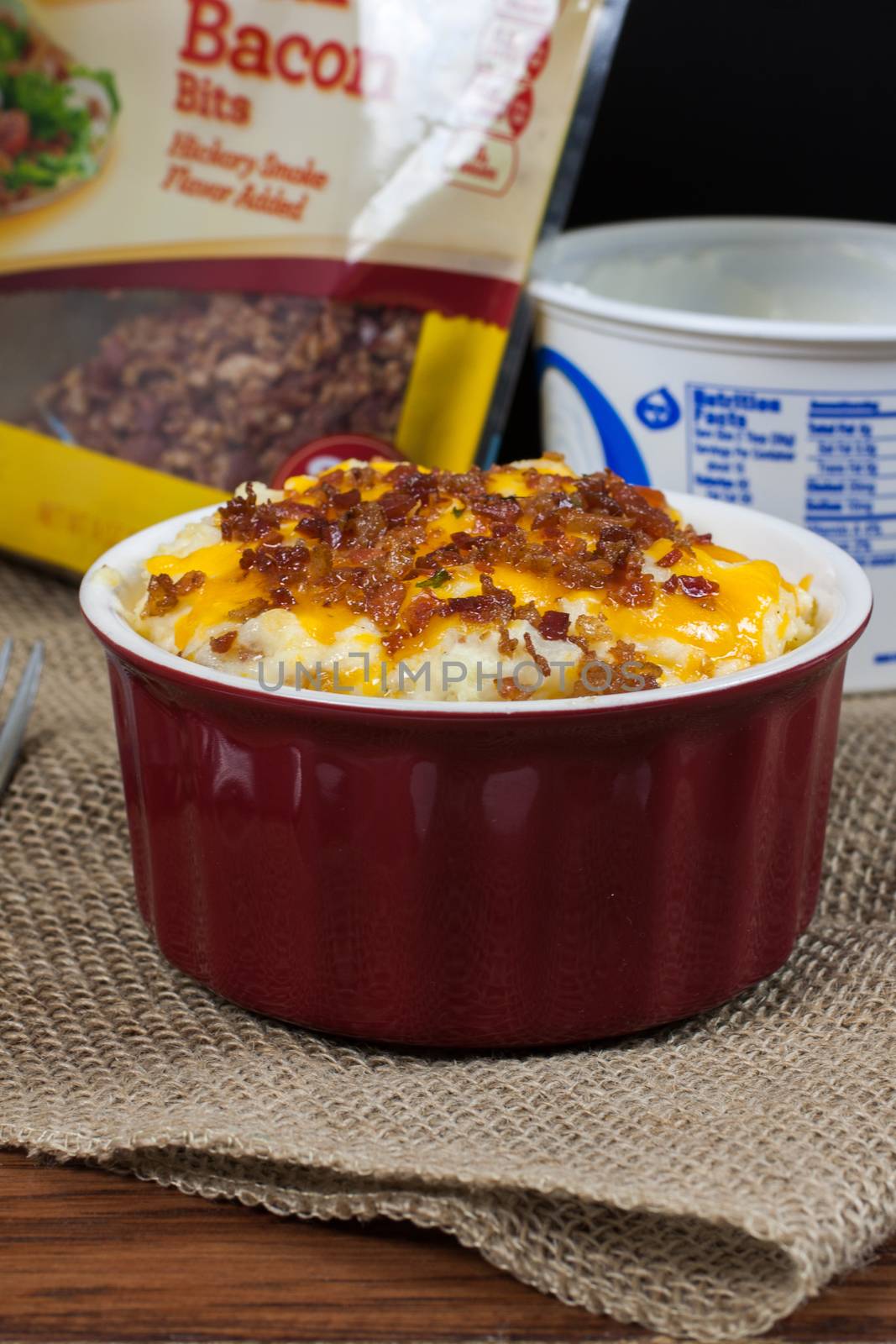 A crock of loaded mashed potatoes with melted cheese and bacon on top.