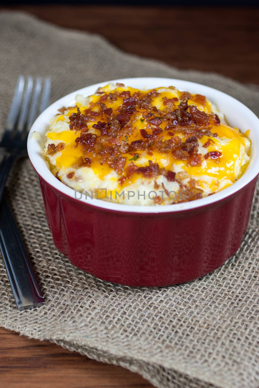 A crock of loaded mashed potatoes with melted cheese and bacon on top.