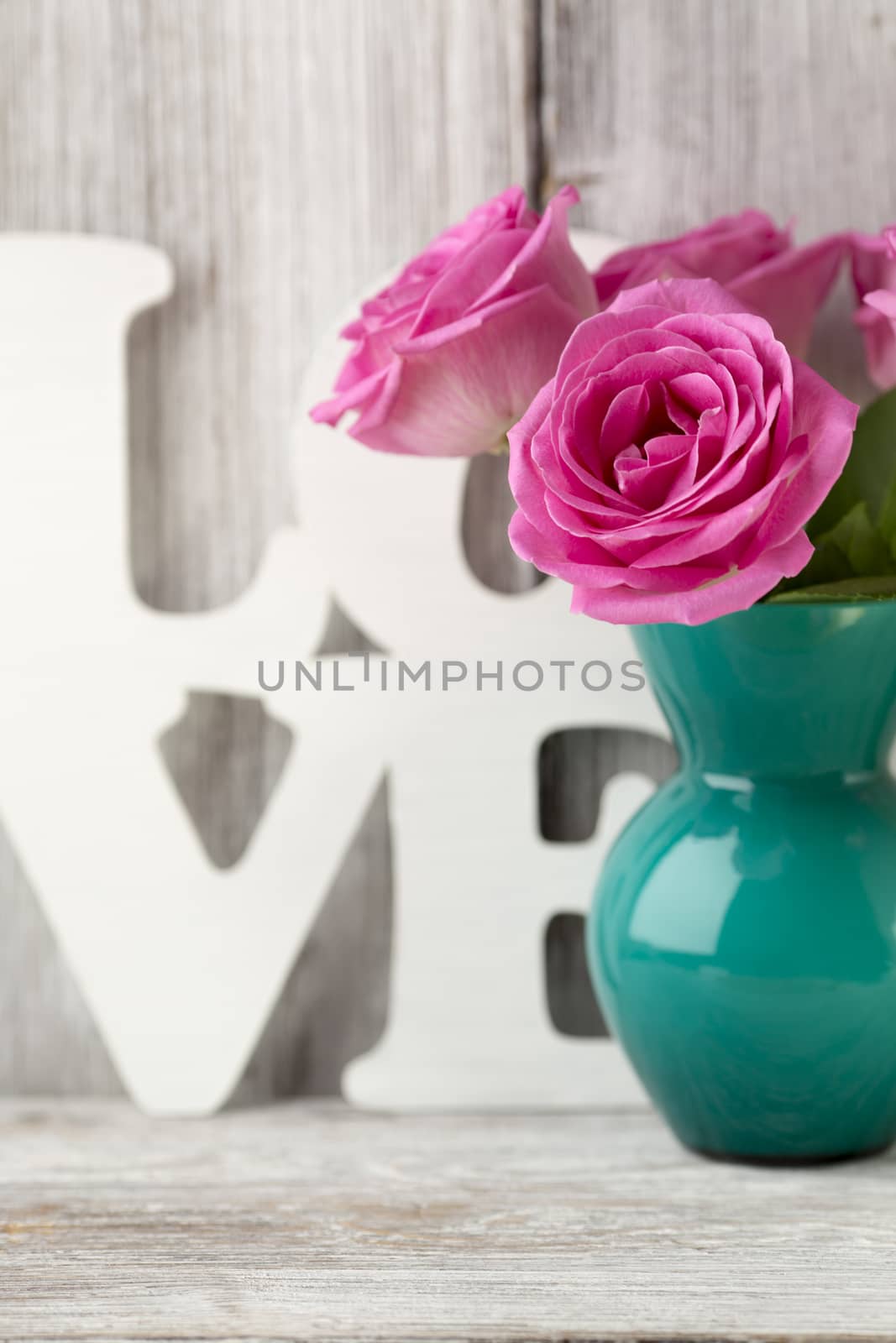 Pink roses in a vase with a Valentine's Day decoration on a wooden shelf.