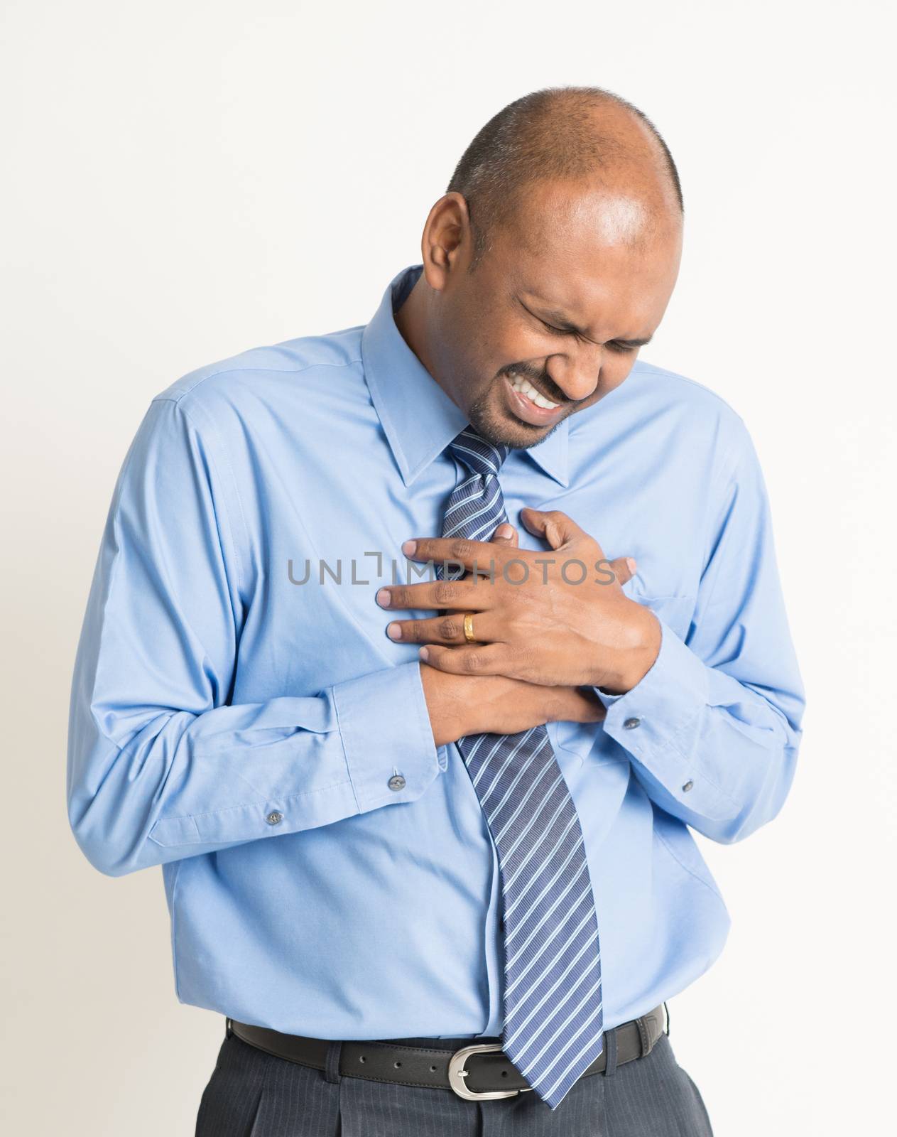 Indian businessman heartache, pressing on chest with painful expression, on plain background