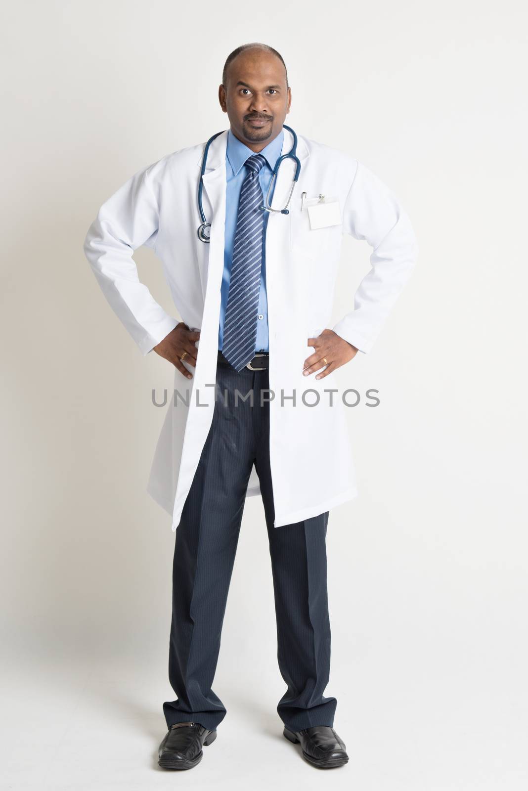 Full length Indian male medical doctor in uniform standing on plain background with shadow. 